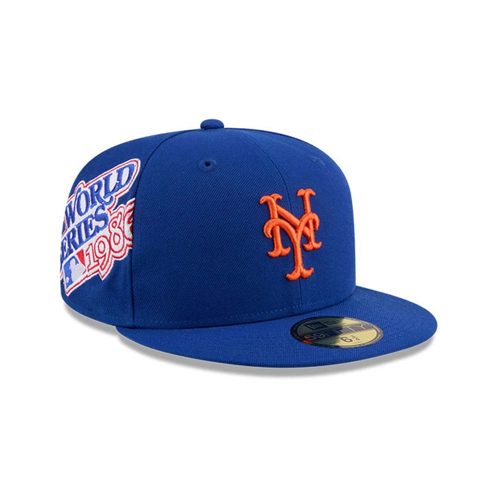 New York Mets MLB Hidden Hit Blue New Era 59FIFTY Fitted Cap, three-quarter view showing the orange embroidered Mets logo on the front panel, a 1986 World Series patch on the side, and a gold 59FIFTY size sticker on the flat blue visor.