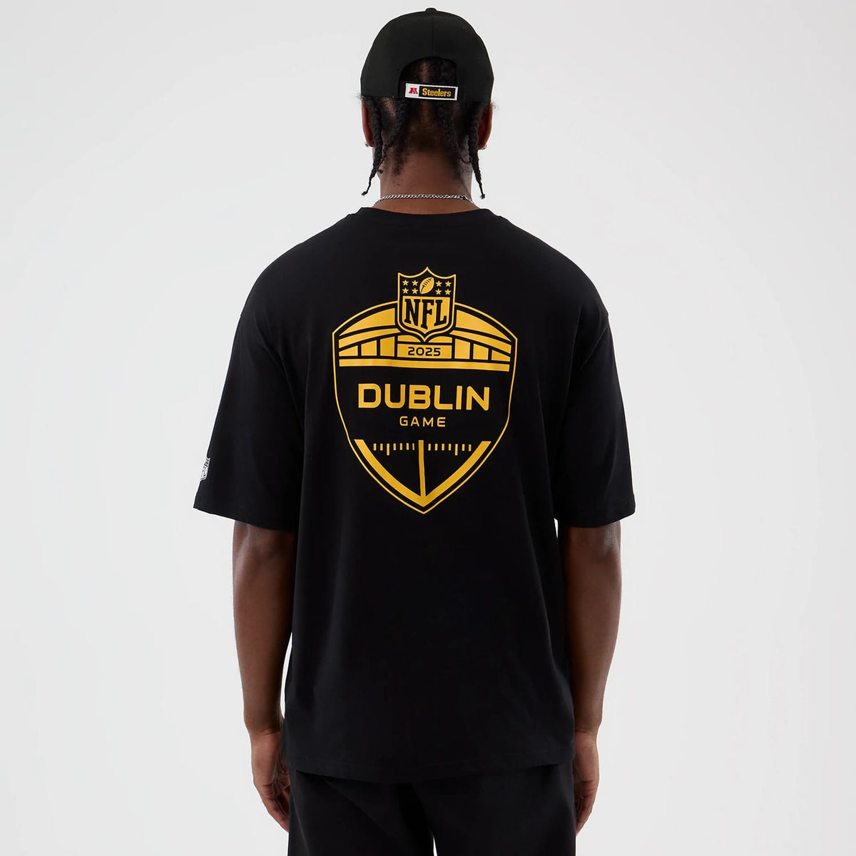 New Era Pittsburgh Steelers NFL International Series Games Black Oversized T-Shirt, back view showing a large yellow NFL Dublin Game 2025 emblem, worn by a model with a matching cap featuring a raised Steelers logo on the back.