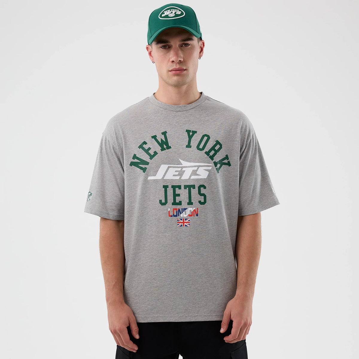 New Era New York Jets NFL International Series Games Grey Oversized T-Shirt, front view on-model showing green New York Jets lettering with a graphic in the centre, a LONDON tag and a small UK flag printed below.