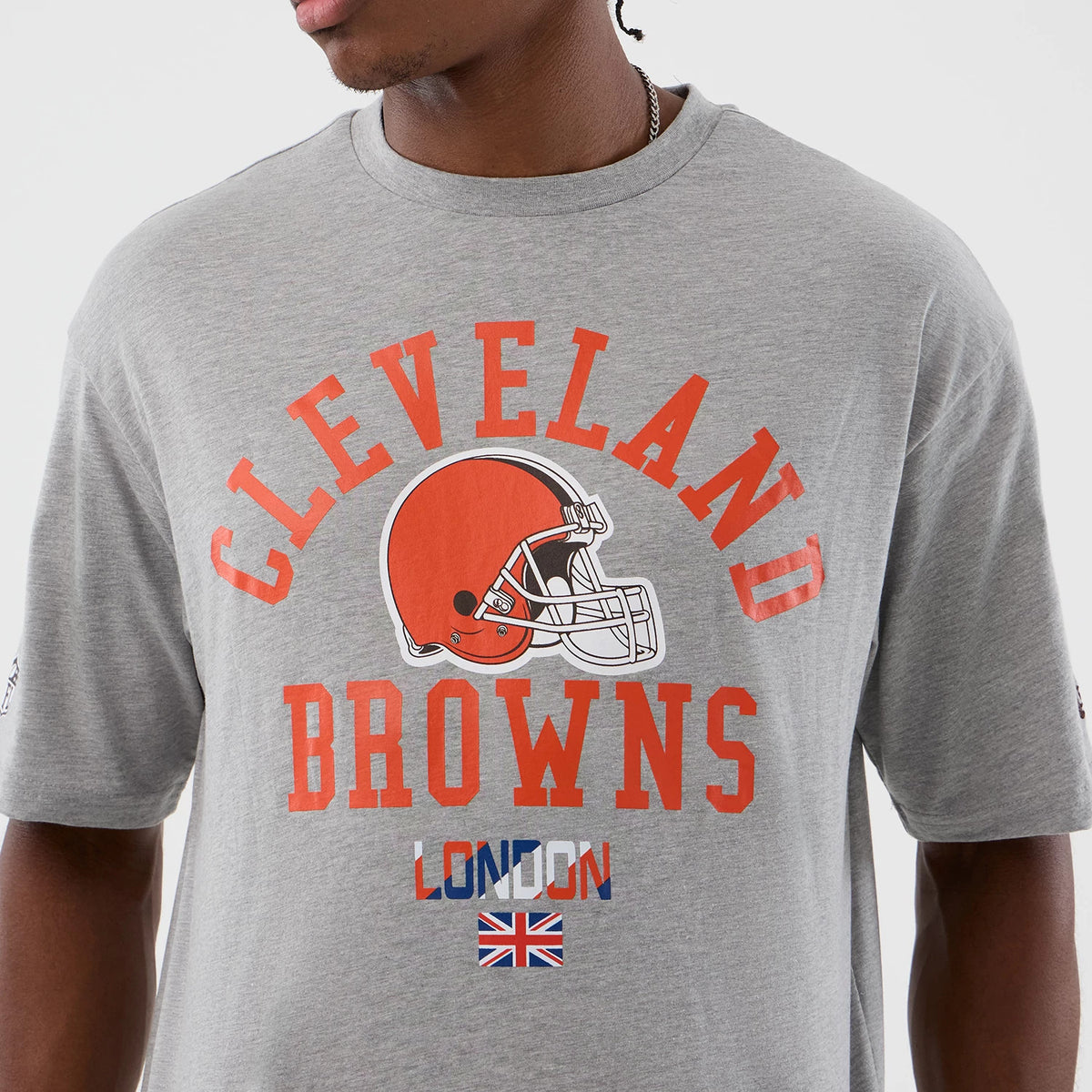 New Era Cleveland Browns NFL International Series Games Grey Oversized T-Shirt, front view showing an orange helmet graphic at the centre with Cleveland Browns lettering above and London text with a Union Jack flag below, worn by a model.