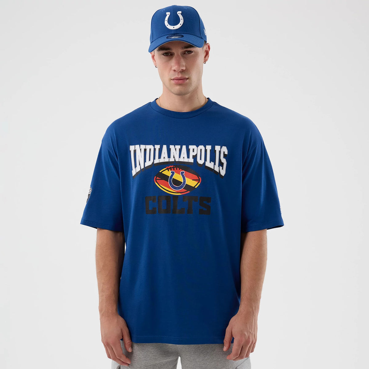 New Era Colts NFL International Series Games Script Blue Oversized T-Shirt, front view on-model displaying INDIANAPOLIS and COLTS text with team logo in the centre and matched with a blue cap featuring a raised team emblem.
