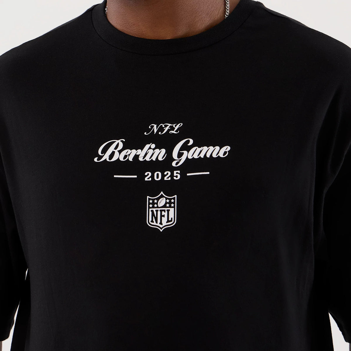 New Era Berlin NFL International Series Games Black Oversized T-Shirt, front view on-model featuring a white printed NFL Berlin Game 2025 graphic and NFL logo centrally positioned on the chest against a black backdrop.