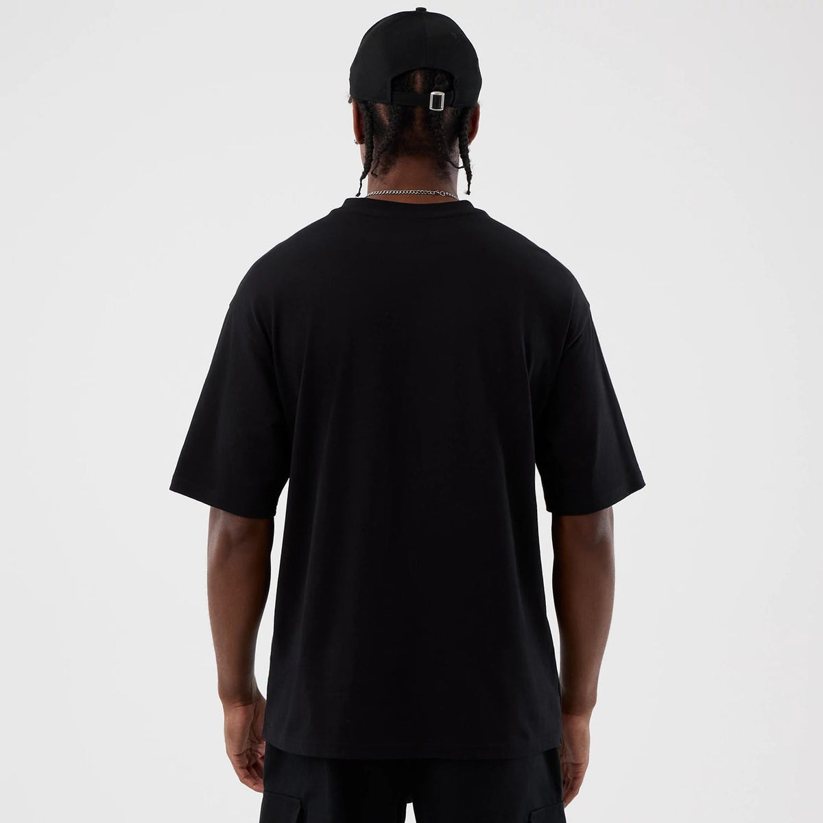 New Era Berlin NFL International Series Games Black Oversized T-Shirt, back view on a model paired with a black cap, showing the plain black rear with a relaxed fit extending below the waist.