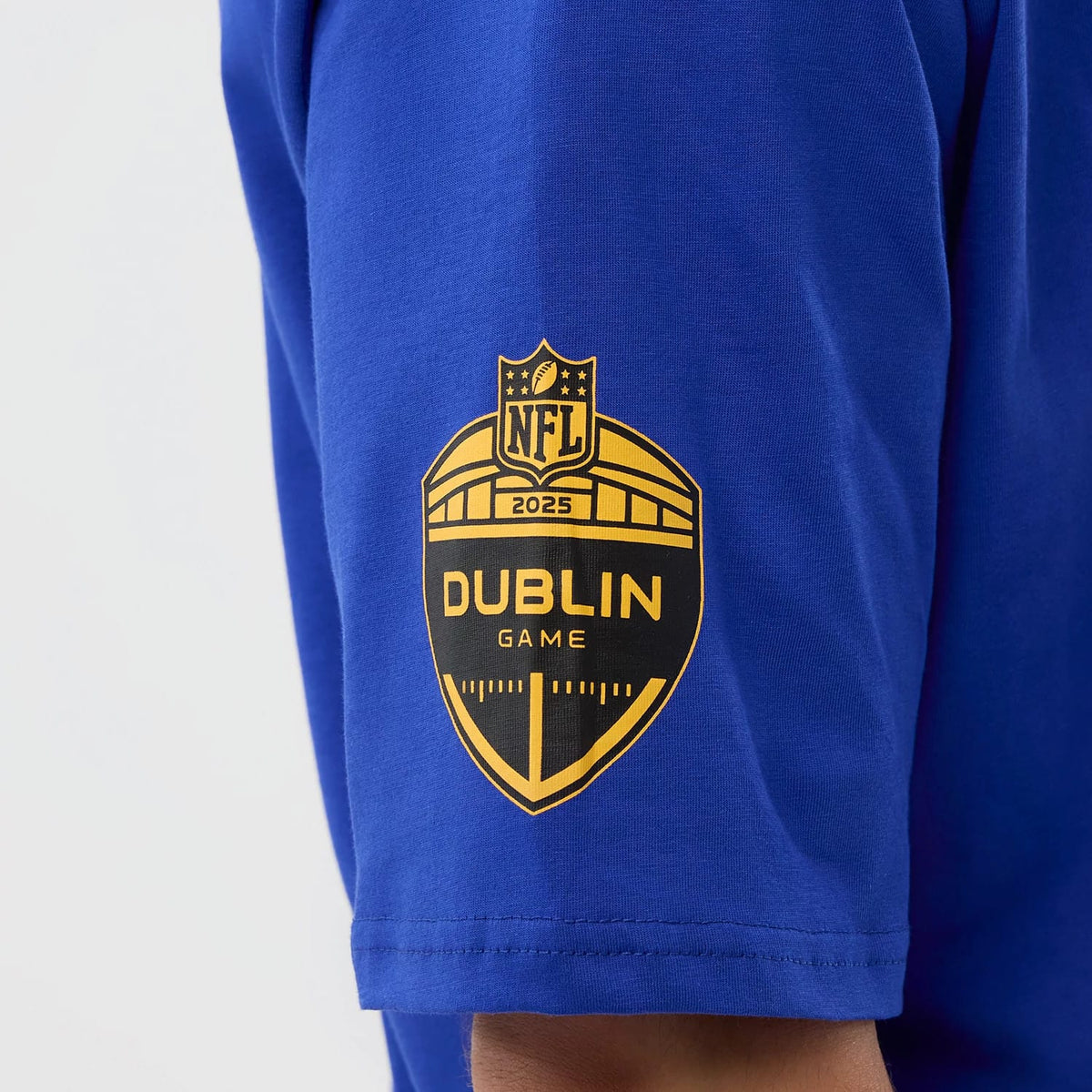 New Era Pittsburgh Steelers NFL International Series Games Blue Oversized T-Shirt, side view revealing a printed golden Dublin Game 2025 emblem on the sleeve against a vivid blue fabric.
