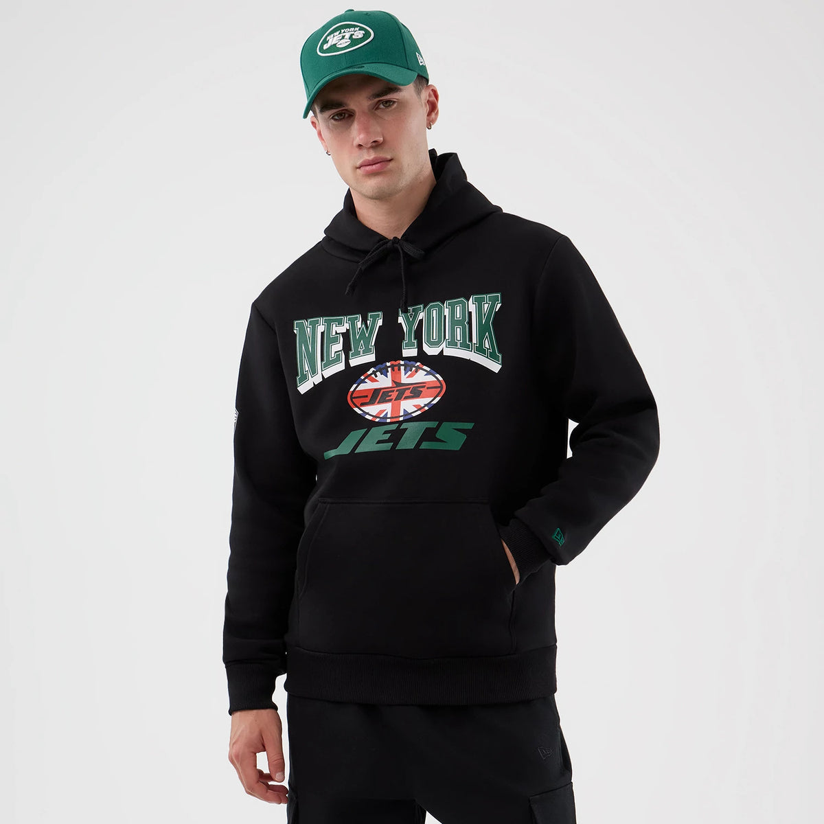 New Era New York Jets NFL International Series Games Black Pullover Hoodie, front view on-model displaying a large graphic with New York in green letters above a stylised ball emblem, a green Jets logo beneath.
