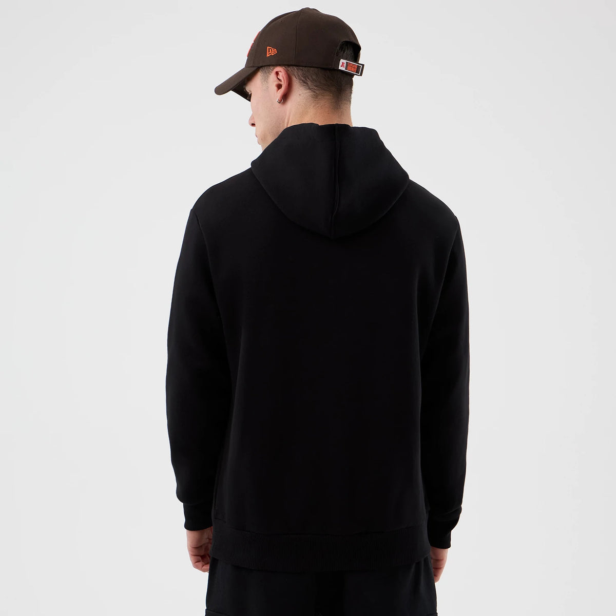 New Era Cleveland Browns NFL International Series Games Black Pullover Hoodie, back view on a model styled with a brown cap, featuring a plain black design with a hood extending from the neckline.