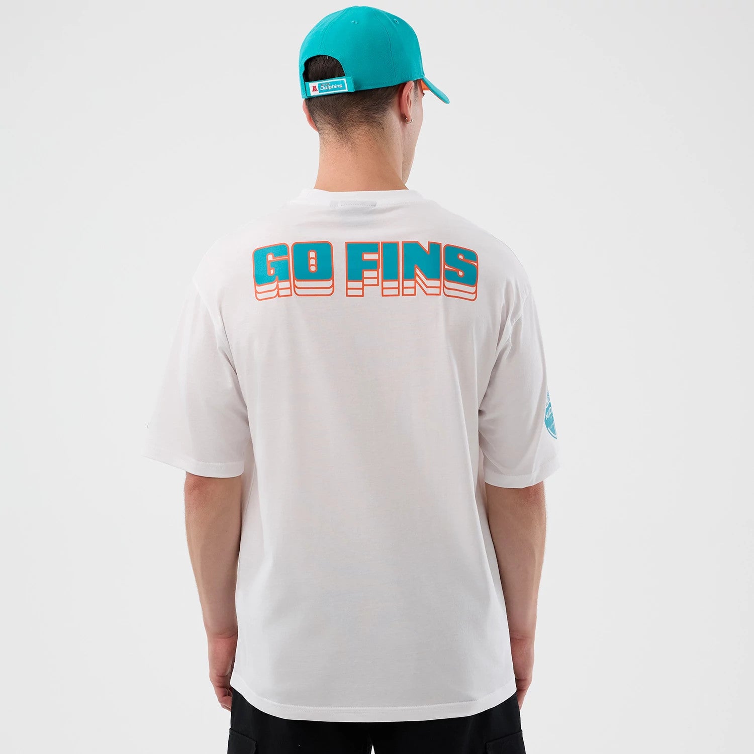 New Era Dolphins NFL International Series Games Madrid White Oversized T-Shirt, back view showing turquoise and orange GO FINS lettering across the upper back, worn by a model with a turquoise cap.