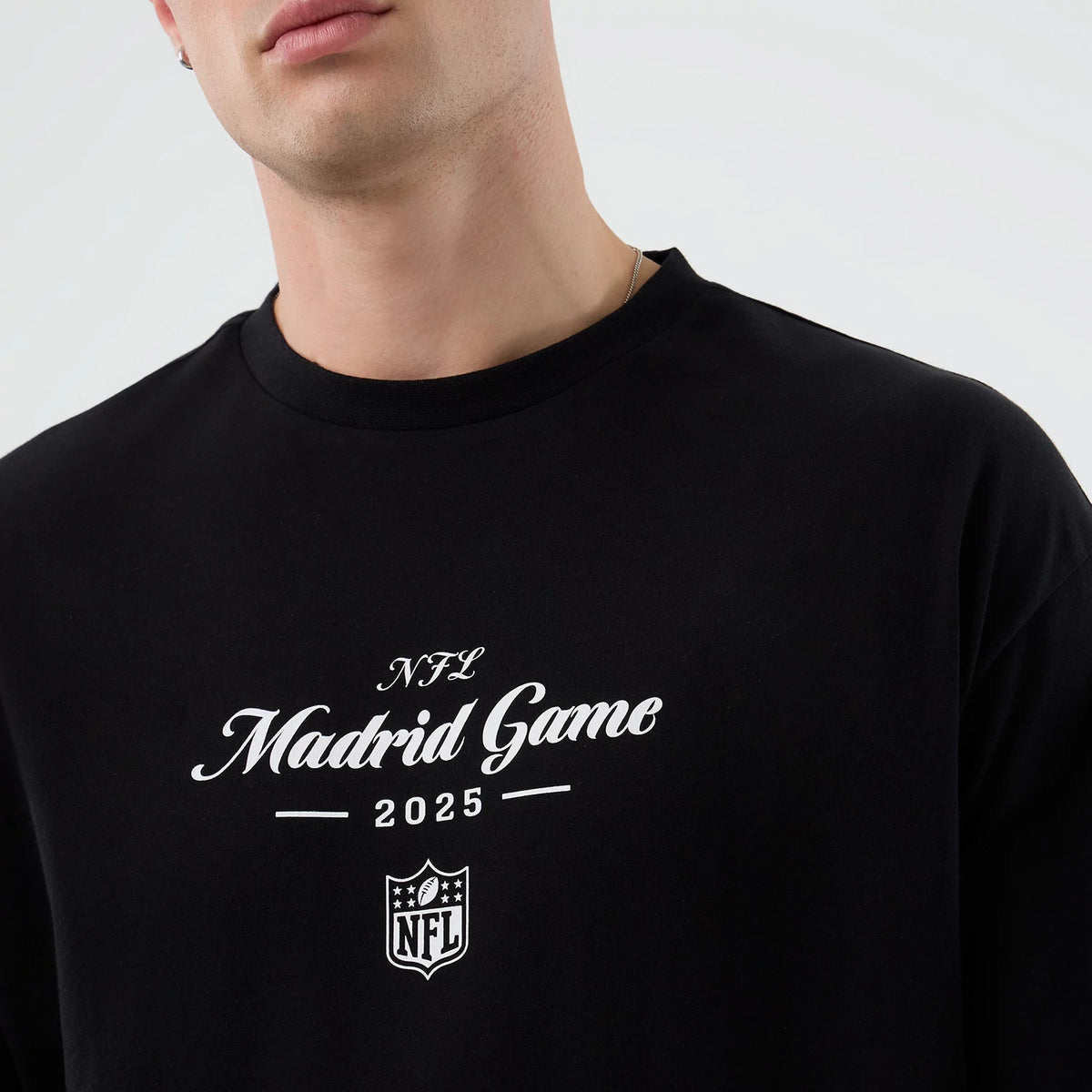 New Era Madrid Game NFL International Series Games Black Oversized T-Shirt, front view on-model displaying white printed lettering NFL Madrid Game 2025 above the NFL shield logo on the chest of the black tee.