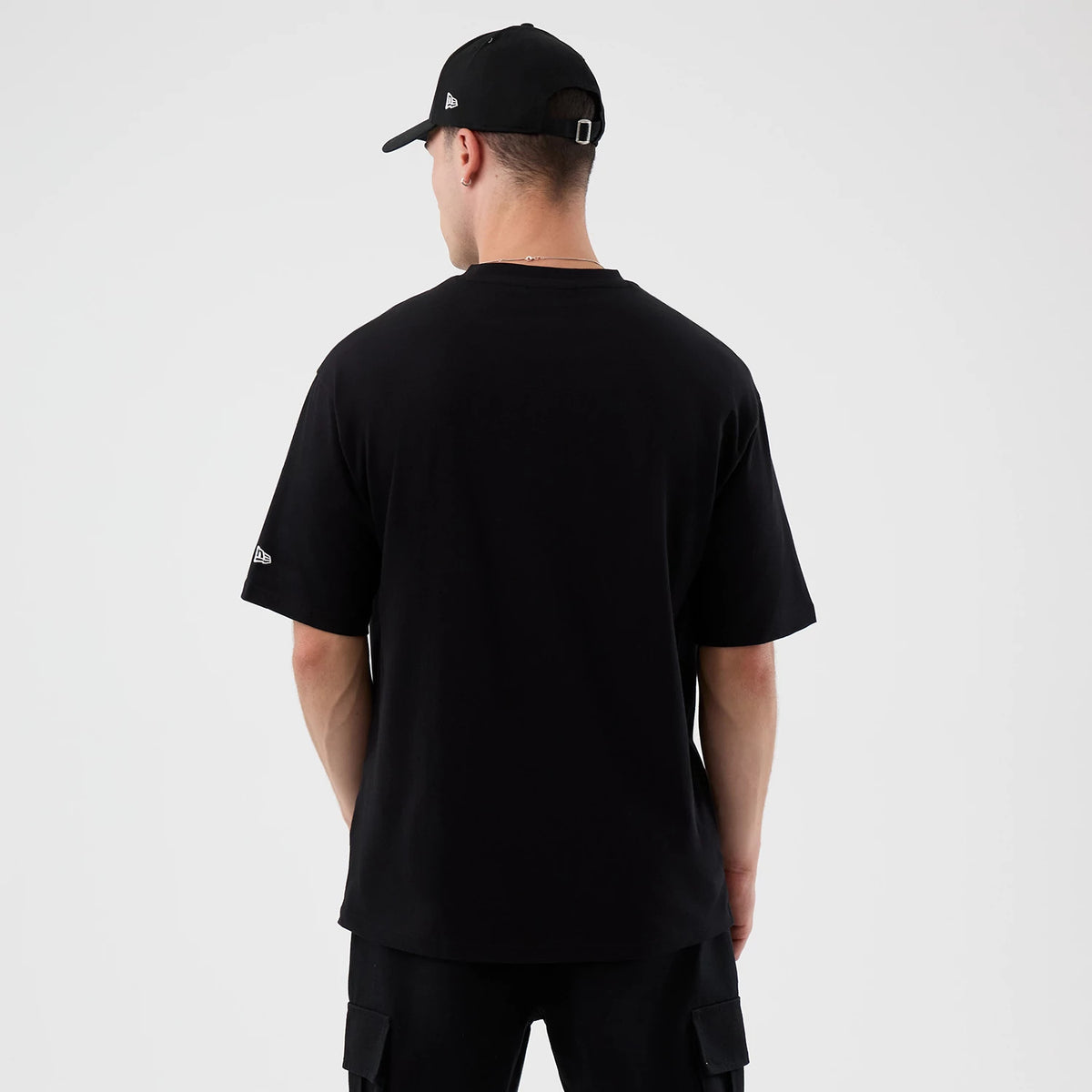 New Era Madrid Game NFL International Series Games Black Oversized T-Shirt, back view on a model showcasing the plain black back with a small embroidered New Era logo on the left sleeve, styled with a matching black cap.