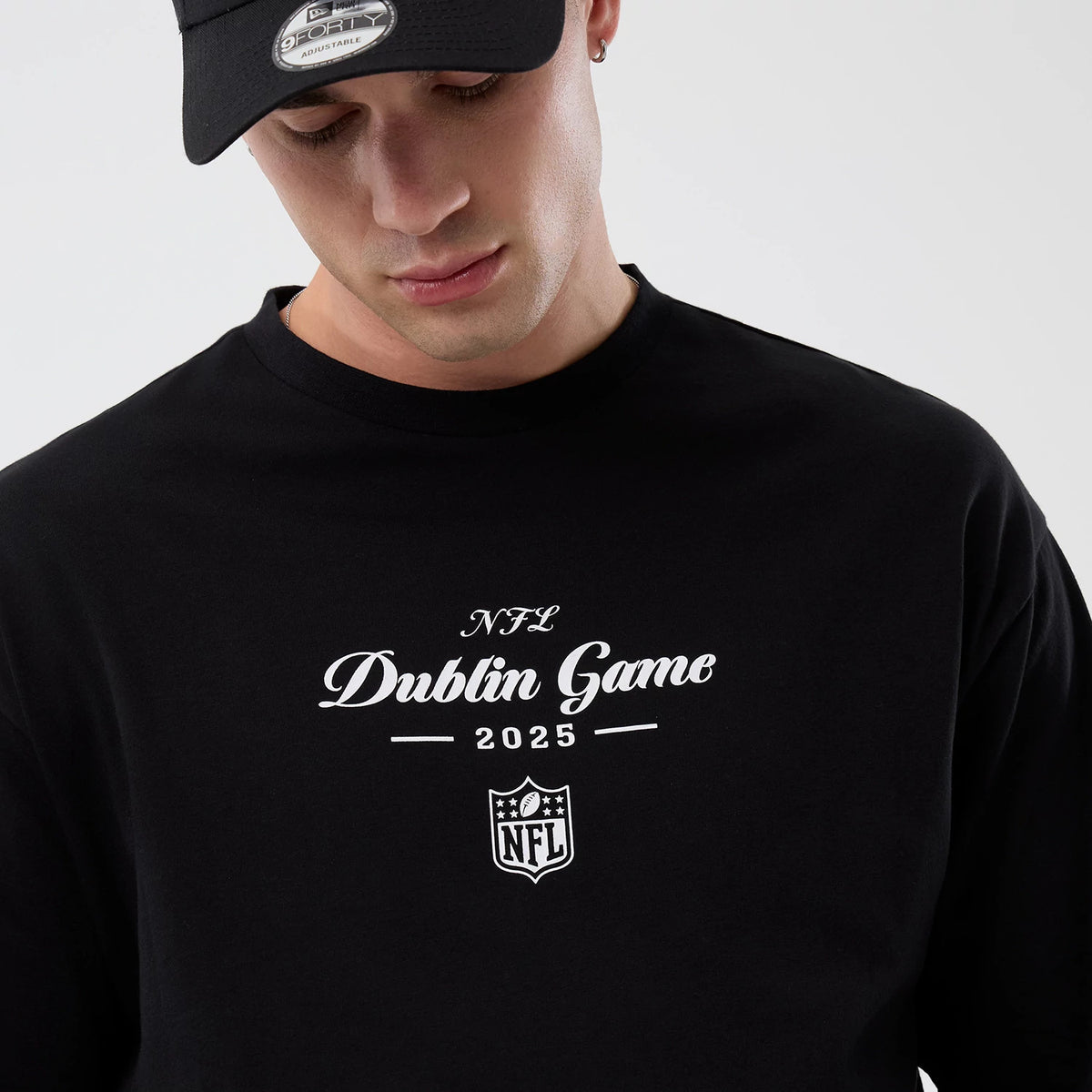 New Era Dublin Game NFL International Series Games Black Oversized T-Shirt, front view on-model showing white NFL Dublin Game 2025 lettering and an NFL shield logo printed centrally on the chest against the black fabric.