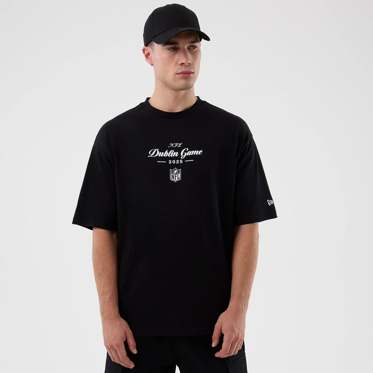 New Era Dublin Game NFL International Series Games Black Oversized T-Shirt, front view on-model showing white printed Dublin Game 2025 lettering and NFL shield logo on the chest, with a small embroidered New Era flag on the left sleeve.