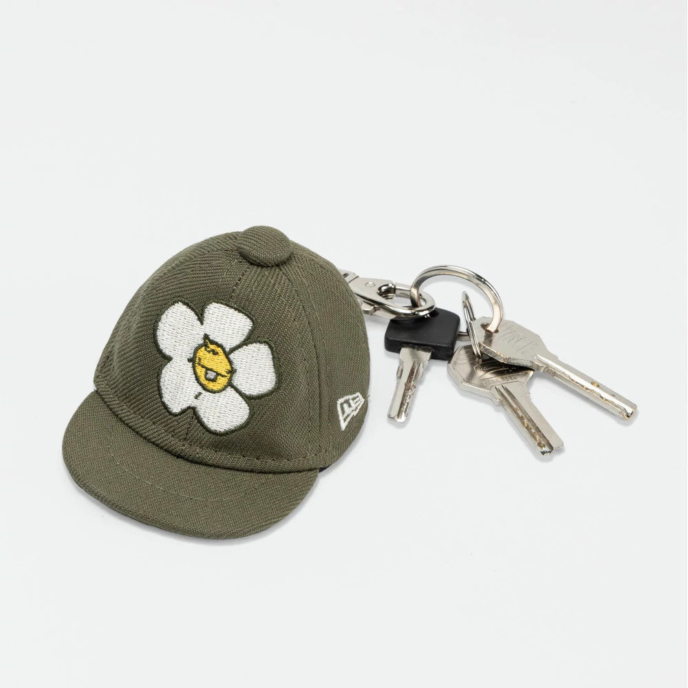 New Era x Rodrigo Roji Flower Green Mini 59FIFTY Fitted Cap, three-quarter view showing the embroidered white flower and yellow face logo on the front panel, with a small visor and New Era flag logo on the left side, attached to keyring with keys.
