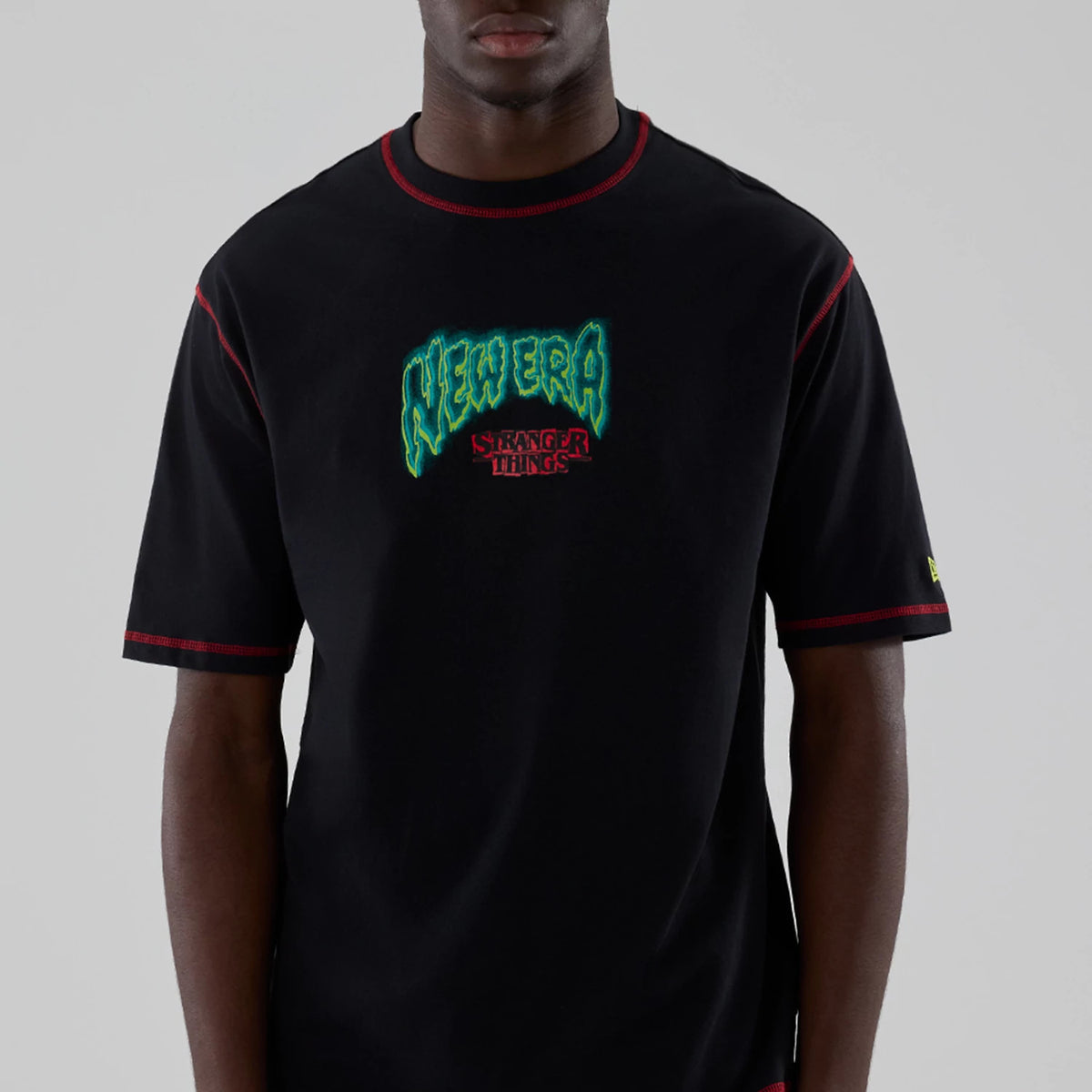 New Era Stranger Things Black Oversized T-Shirt, front view featuring neon green embroidered New Era text above the red embroidered Stranger Things logo, with red stitching on the sleeves and neckline, worn by a model.