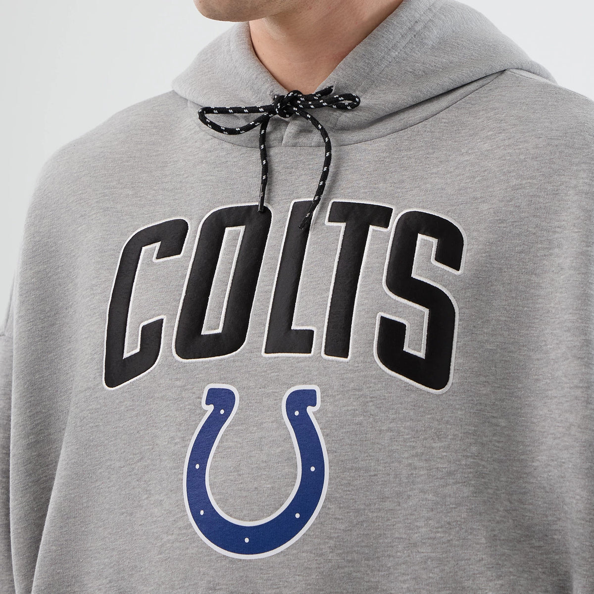 New Era Indianapolis Colts NFL International Series Games Grey Pullover Hoodie, front view on-model showing black COLTS lettering across the chest above a large blue horseshoe logo, with a black drawstring across the hood.