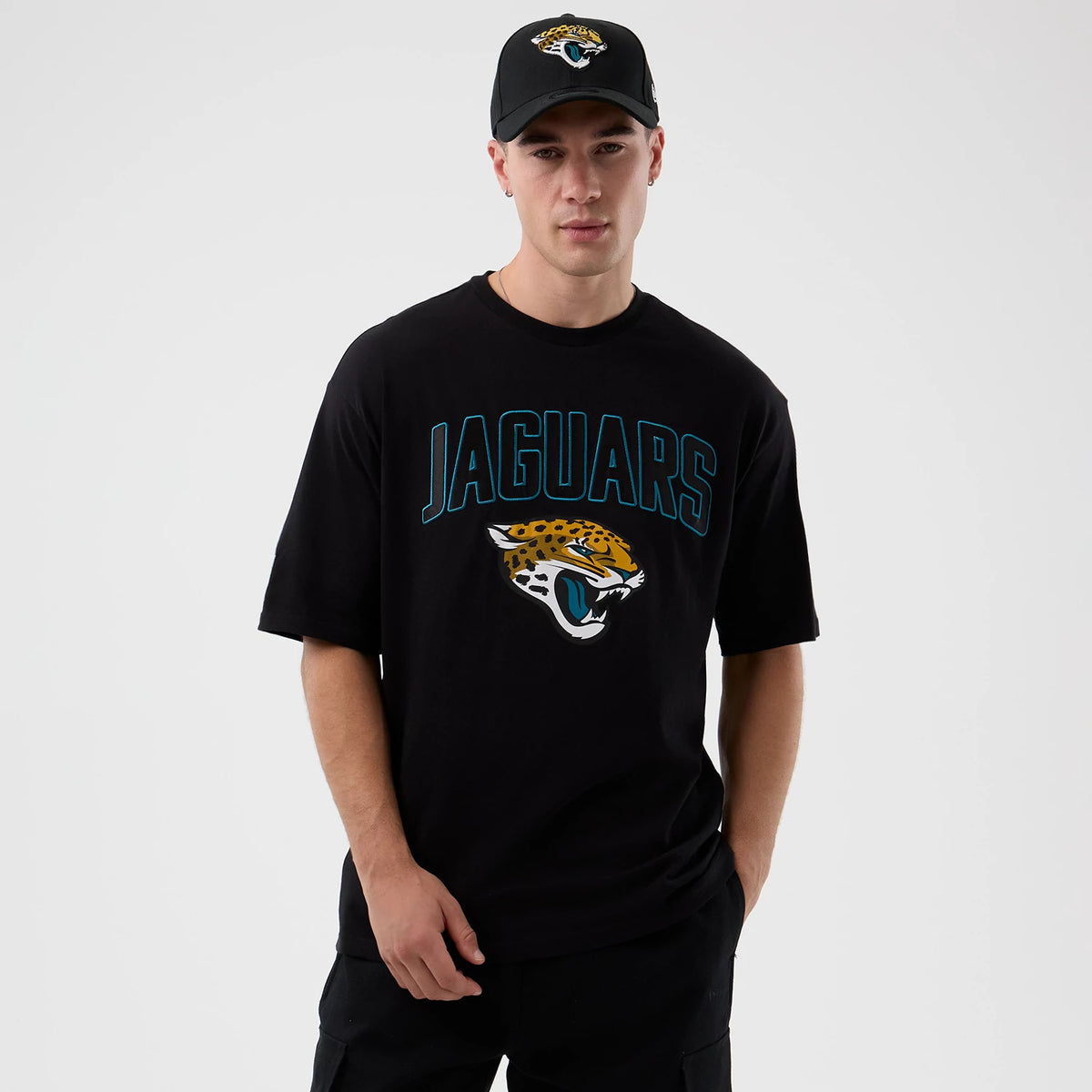 New Era Jaguars NFL International Series Games Script Black Oversized T-Shirt, front view on-model showing teal Jaguars script across the chest above the fierce embroidered Jaguar head logo, styled with a matching cap.