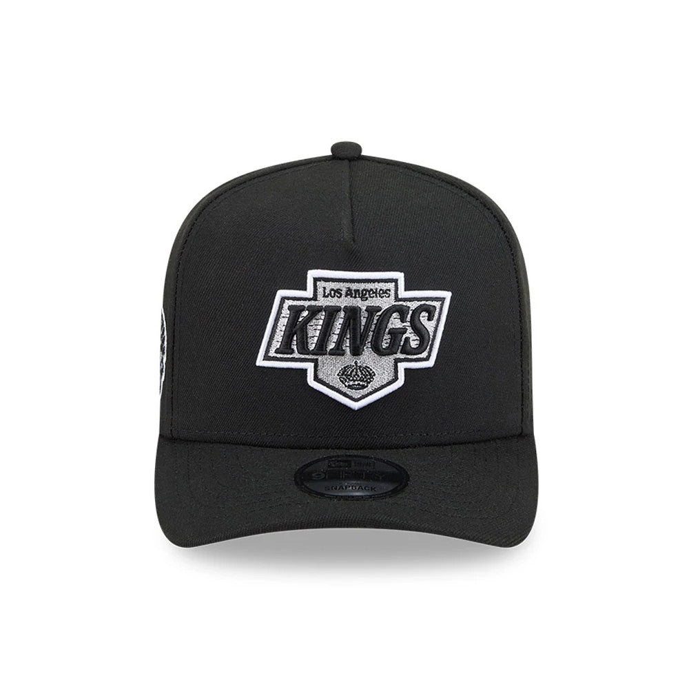 LA Kings NHL Evergreen Black New Era 9FIFTY A-Frame Snapback Adjustable Cap, front view showing a raised embroidered grey and black Los Angeles Kings logo on the crown, with a flat black visor and black 9FIFTY size sticker.