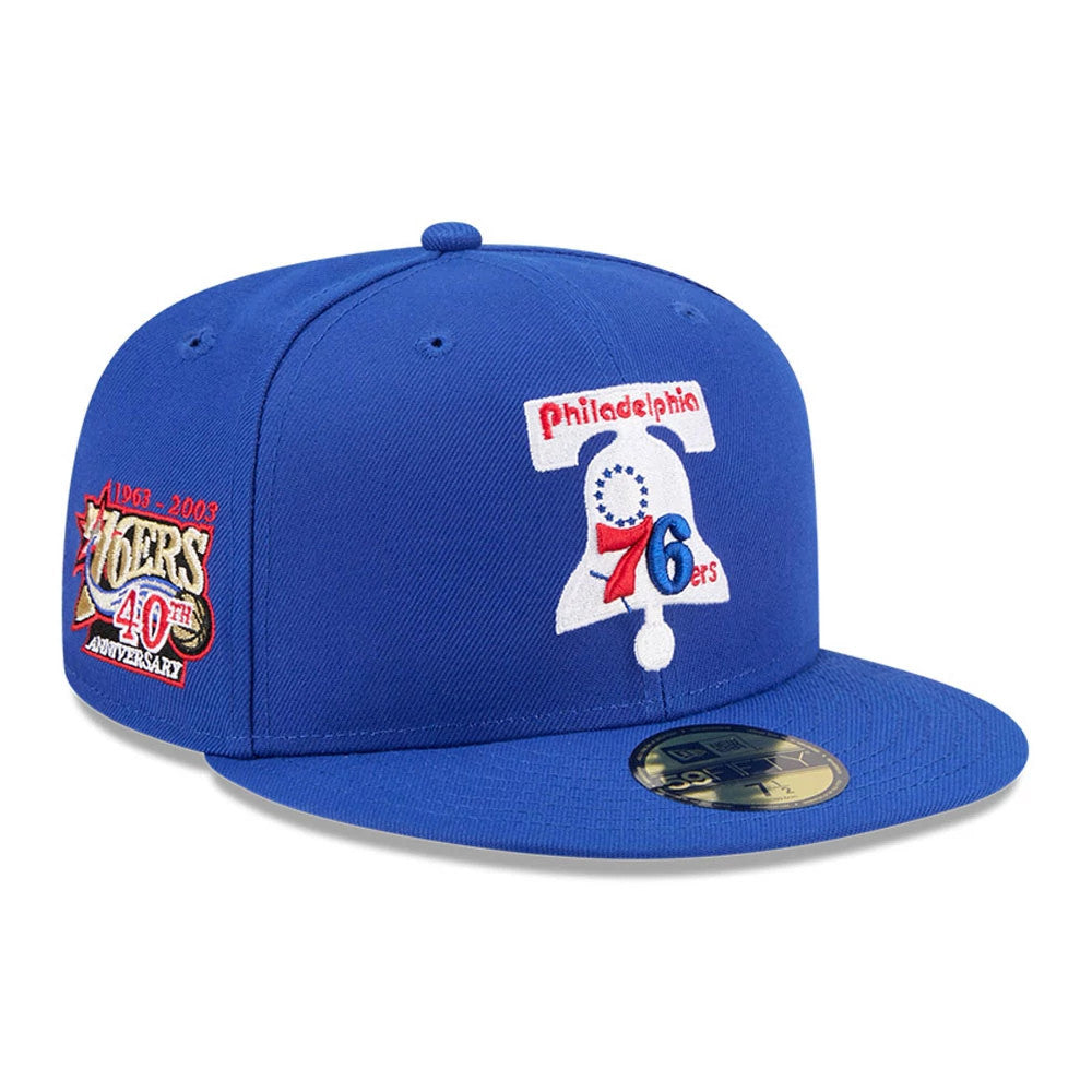 Philadelphia 76ers NBA Hardwood Classic Blue New Era 59FIFTY Fitted Cap, three-quarter view showing a raised embroidered Liberty Bell logo on the front panel with a gold 59FIFTY size sticker on the blue flat visor.