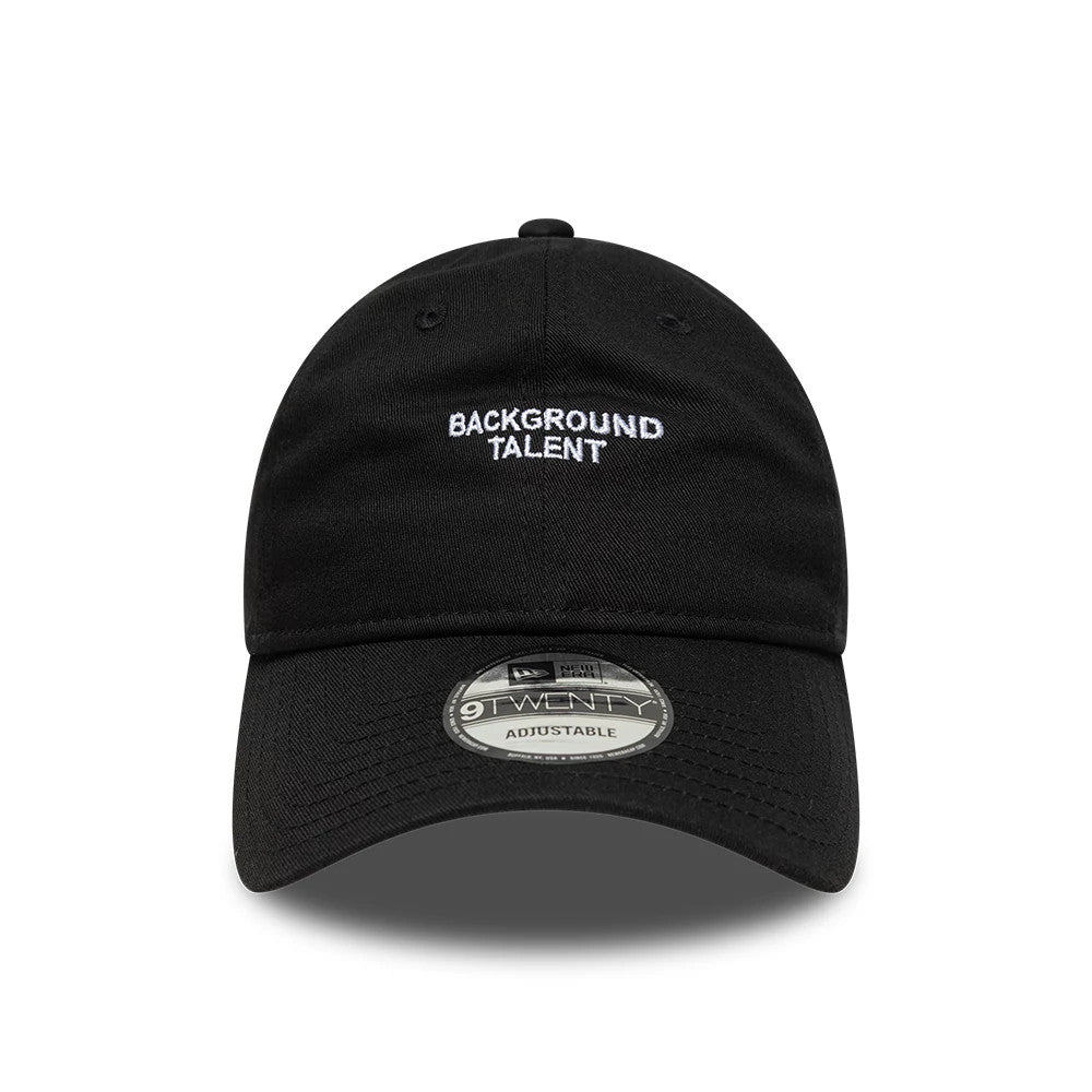 New Era Slogan Background Talent Black 9TWENTY Adjustable Cap, front view showing white embroidered BACKGROUND TALENT text on the centre of the black crown and a 9TWENTY size sticker on the curved black visor.