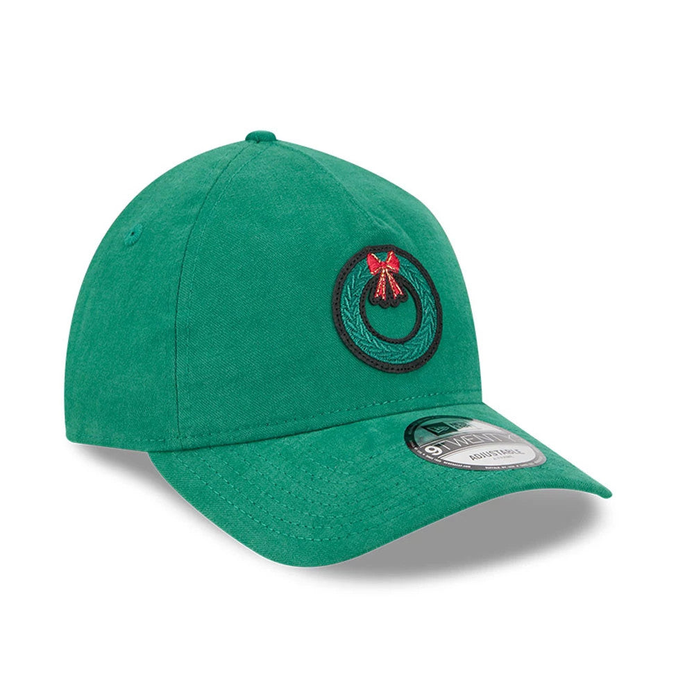 New Era Holiday Essentials Green 9TWENTY A-Frame Adjustable Cap, three-quarter view showing a black wreath logo with a red bow embroidered on the front panel, complemented by the curved green visor and 9TWENTY size sticker.