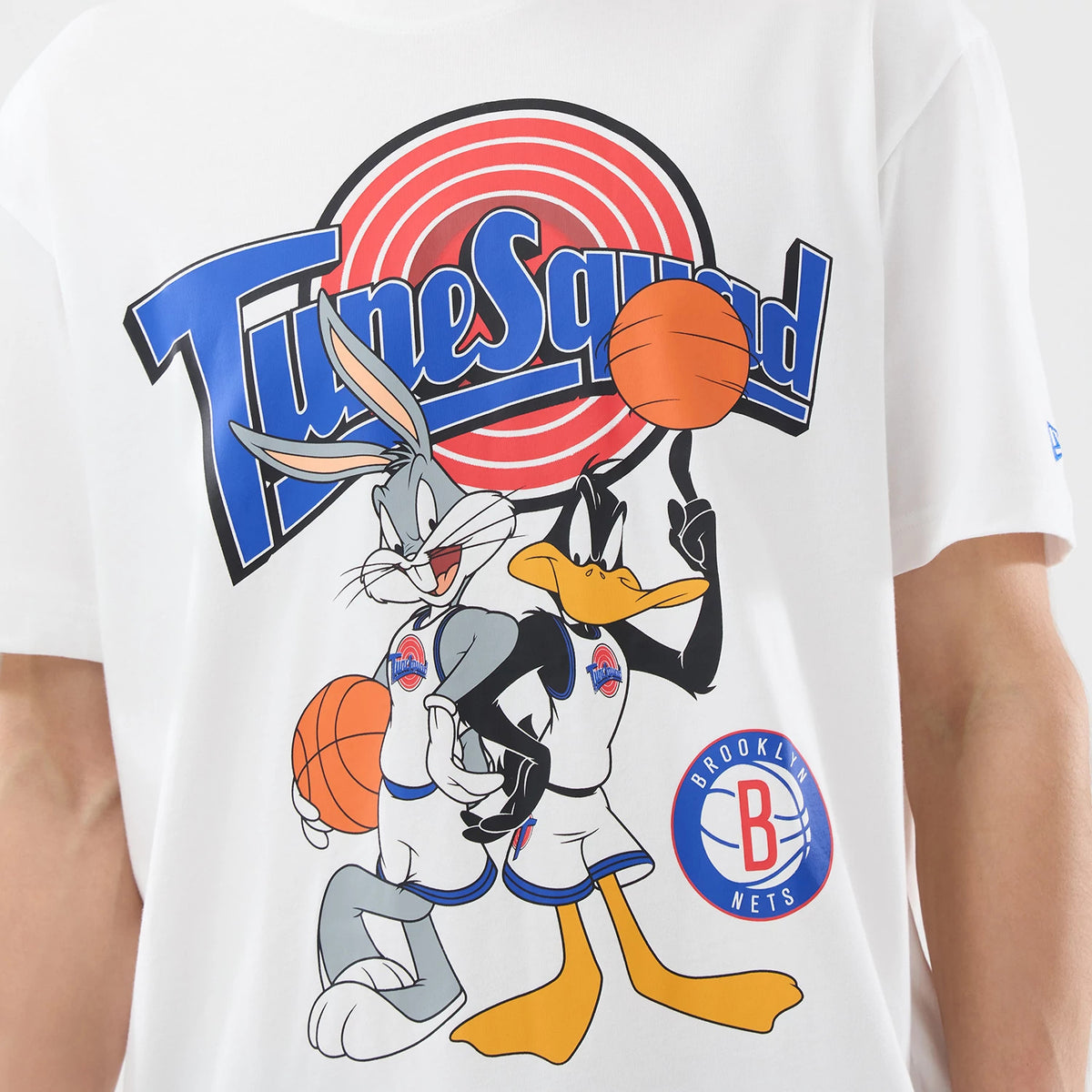 New Era Brooklyn Nets Space Jam 2 X NBA White T-Shirt, front view featuring a large Tune Squad graphic with Bugs Bunny and Daffy Duck holding basketballs, a red and blue logo underneath, and an embroidered New Era logo on the sleeve.