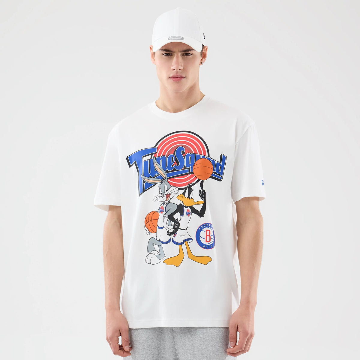 New Era Brooklyn Nets Space Jam 2 X NBA White T-Shirt, front view on-model showing a large printed Tune Squad graphic with Bugs Bunny and Daffy Duck holding basketballs, and the Brooklyn Nets logo in blue and red near the hem.