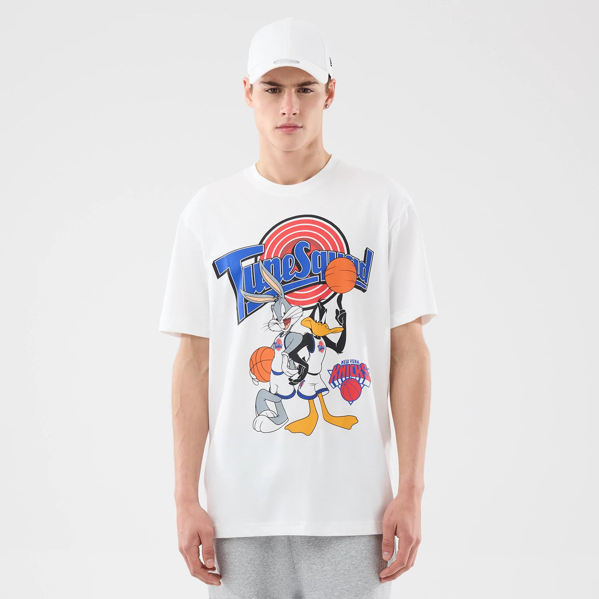 New Era New York Knicks Space Jam 2 X NBA White T-Shirt, front view on a model wearing a white cap, featuring a large printed Tune Squad graphic with Bugs Bunny and Daffy Duck holding basketballs, and the New York Knicks logo at the bottom.