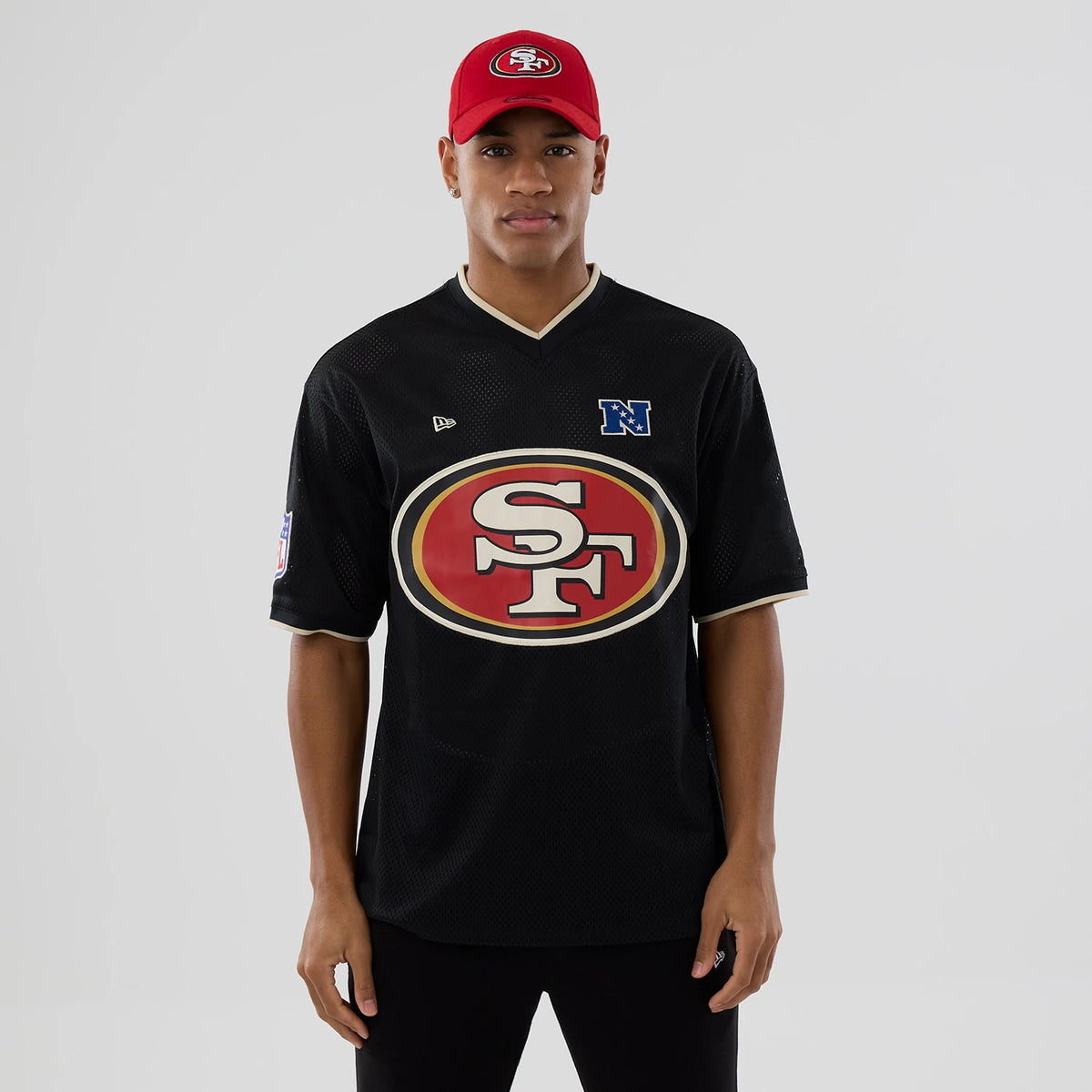 New Era San Francisco 49ers NFL Mesh Black Oversized T-Shirt, front view featuring a large red and gold 49ers logo centred on the chest, an embroidered New Era logo on the upper left chest, styled on a model with a red cap.