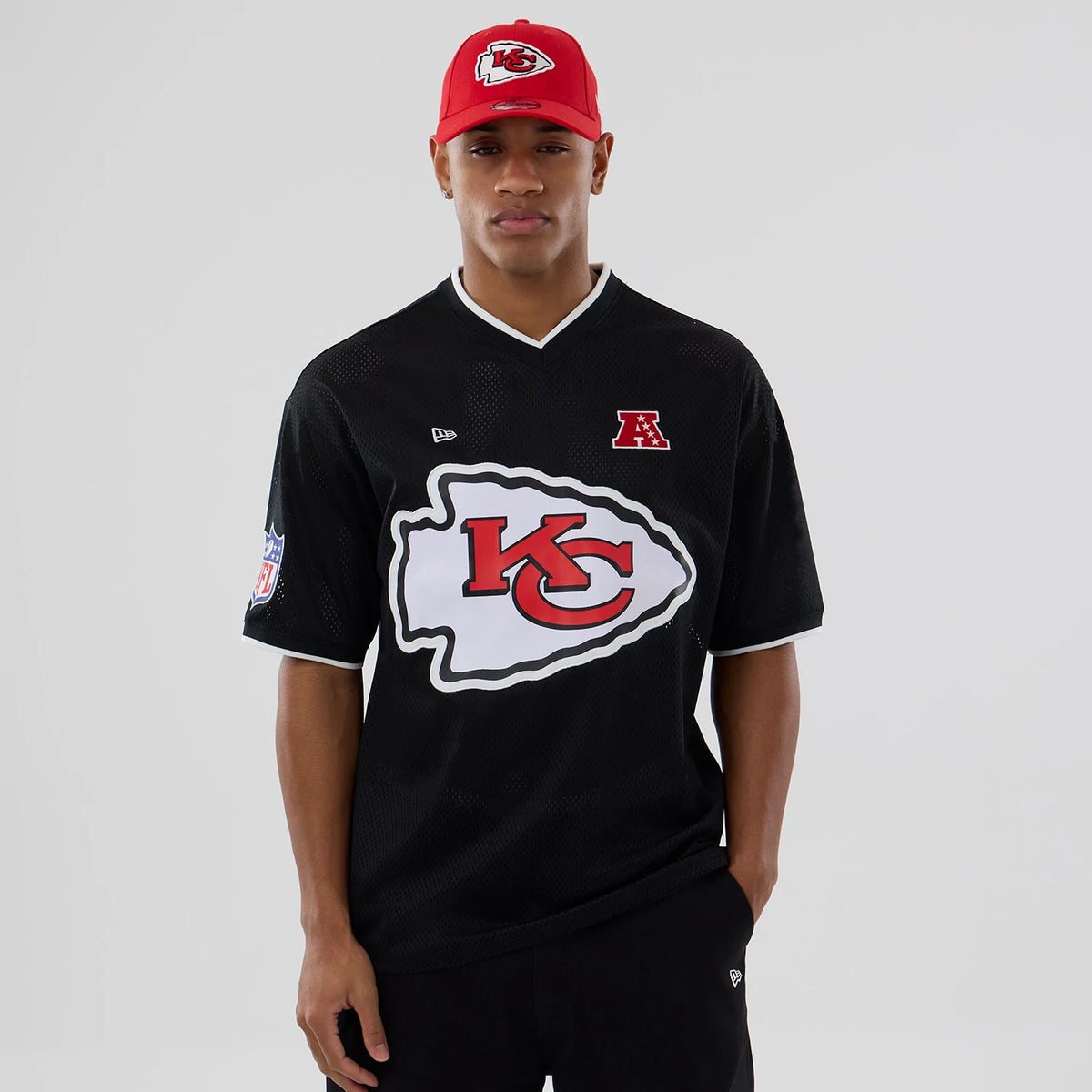 New Era Kansas City Chiefs NFL Mesh Black Oversized T-Shirt, front view on a model with a red cap, featuring a large white and red KC Chiefs logo printed across the chest, an embroidered New Era logo on the upper chest.