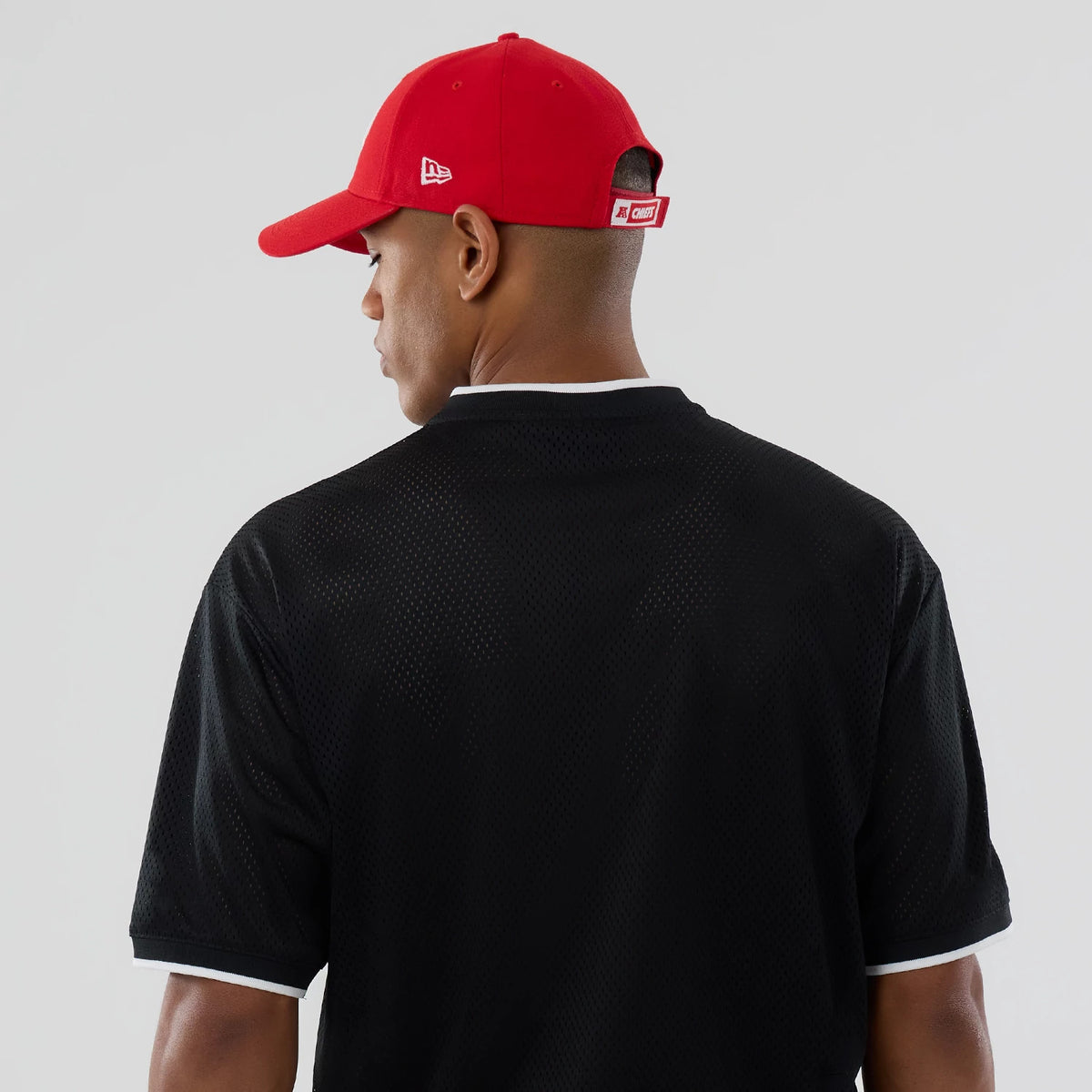 New Era Kansas City Chiefs NFL Mesh Black Oversized T-Shirt, back view on-model paired with a red cap, showcasing the plain black mesh with white trim around the collar and sleeves.