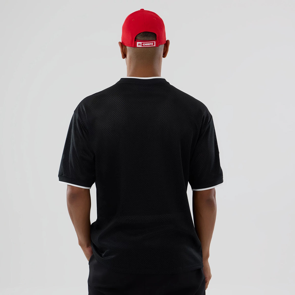 New Era Kansas City Chiefs NFL Mesh Black Oversized T-Shirt, back view showing the plain black mesh with white trim on a model styled with a red cap, highlighting the shirt's loose fit and minimalistic design.
