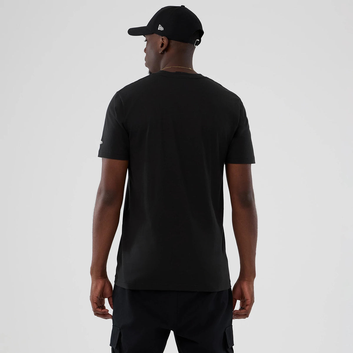 New Era Phoenix Suns NBA Hardwood Classic Black T-Shirt, back view showing a plain black design with short sleeves and an embroidered New Era logo near the left sleeve hem, styled on a model with matching black shorts and cap.