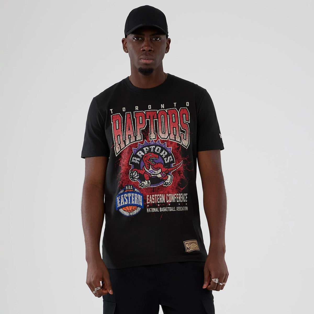 New Era Toronto Raptors NBA Hardwood Classic Black T-Shirt, front view on-model showing the red and white Raptors logo and lettering across the chest, with a woven patch near the hem and a small embroidered New Era logo on the sleeve.