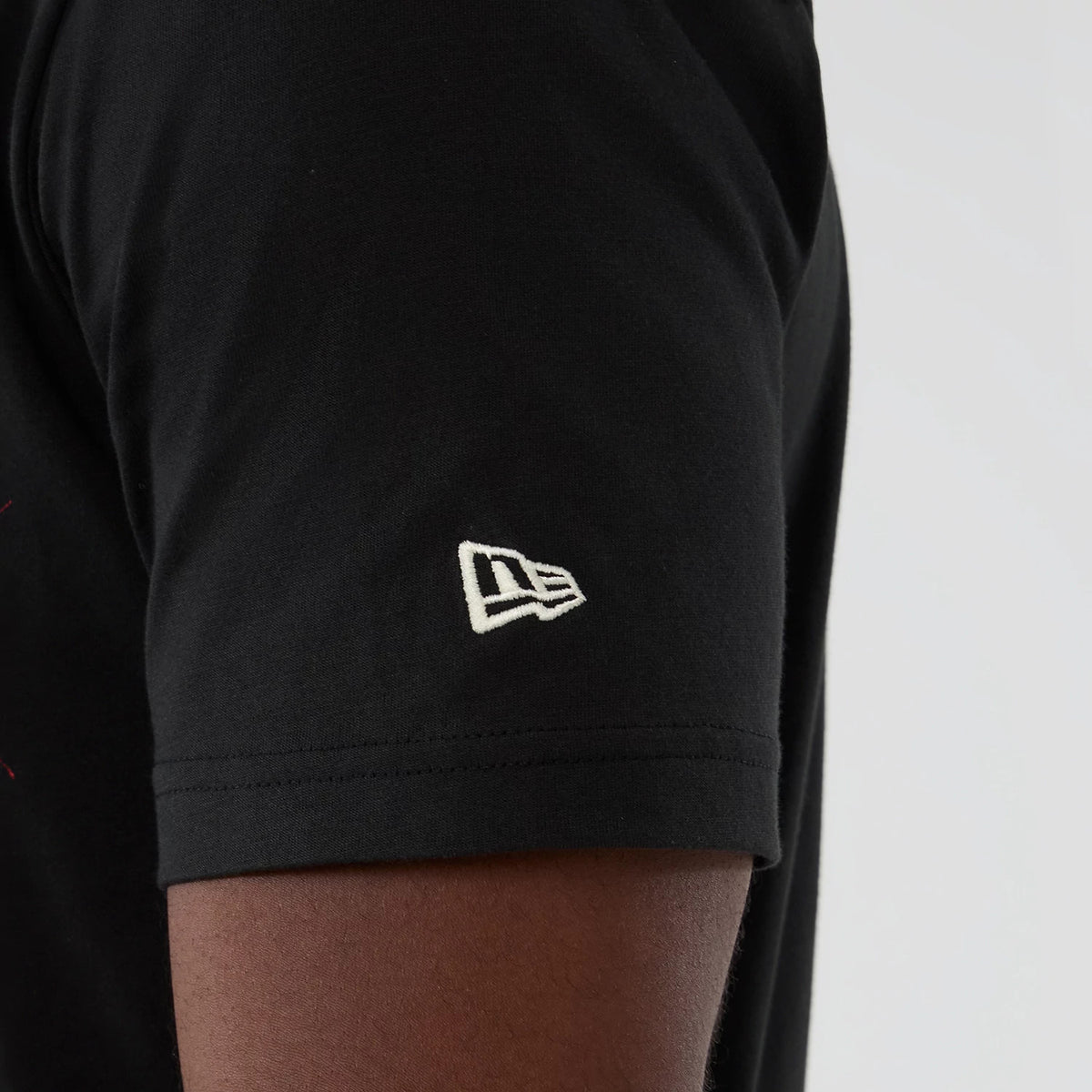New Era Toronto Raptors NBA Hardwood Classic Black T-Shirt, side view showing a close-up of the short sleeve with an embroidered New Era logo in white near the hem on the plain black fabric.
