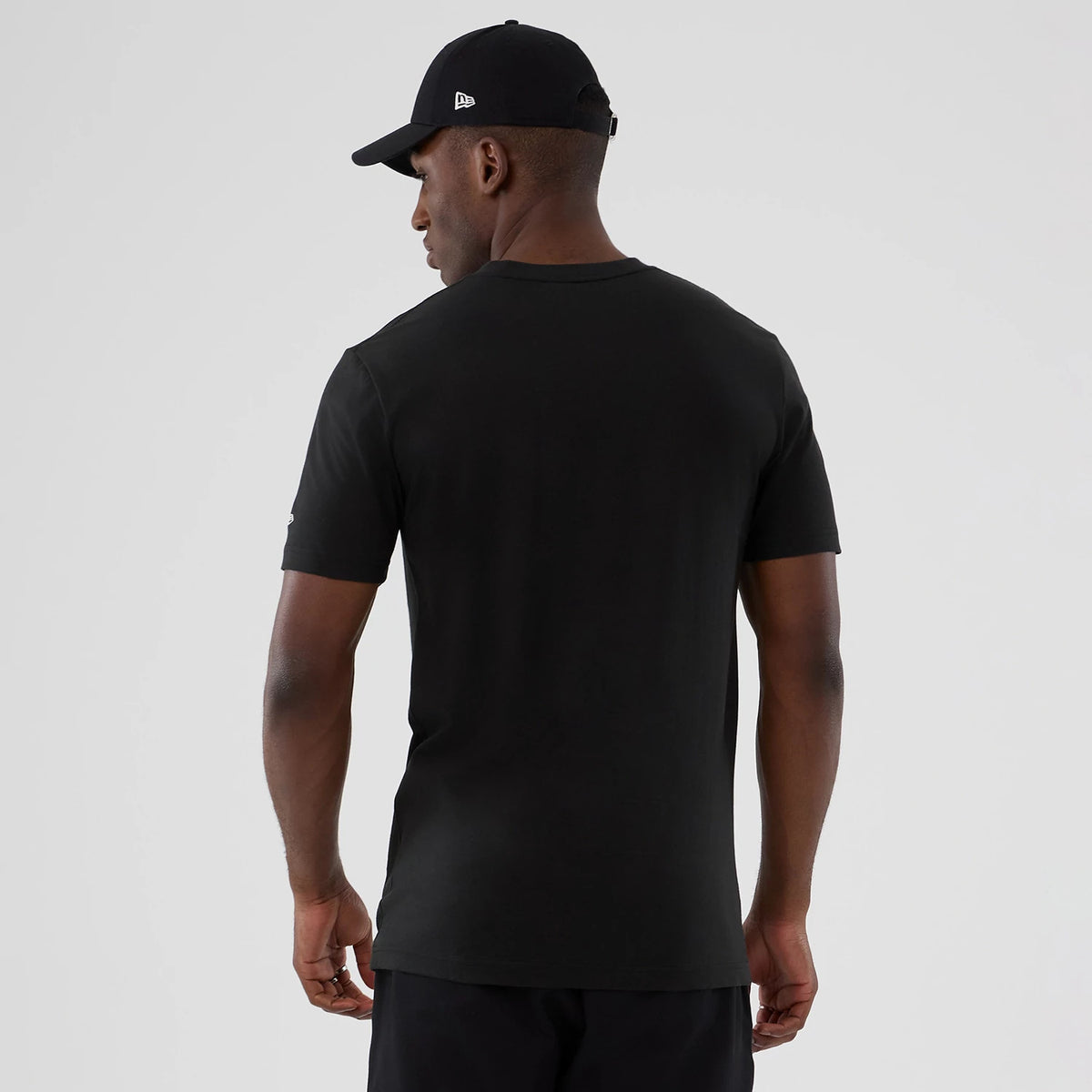 New Era Philadelphia 76ers NBA Hardwood Classic Black T-Shirt, back view showing the plain black back on a model, with short sleeves and a modest round neckline, paired with a black cap featuring an embroidered New Era logo on the side.