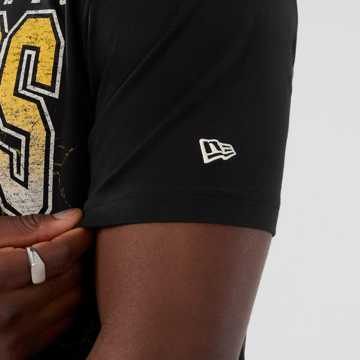 New Era LA Lakers NBA Hardwood Classic Black T-Shirt, side view showing a large graphic with yellow and white distressed lettering on the chest and an embroidered New Era logo on the sleeve near the hem.