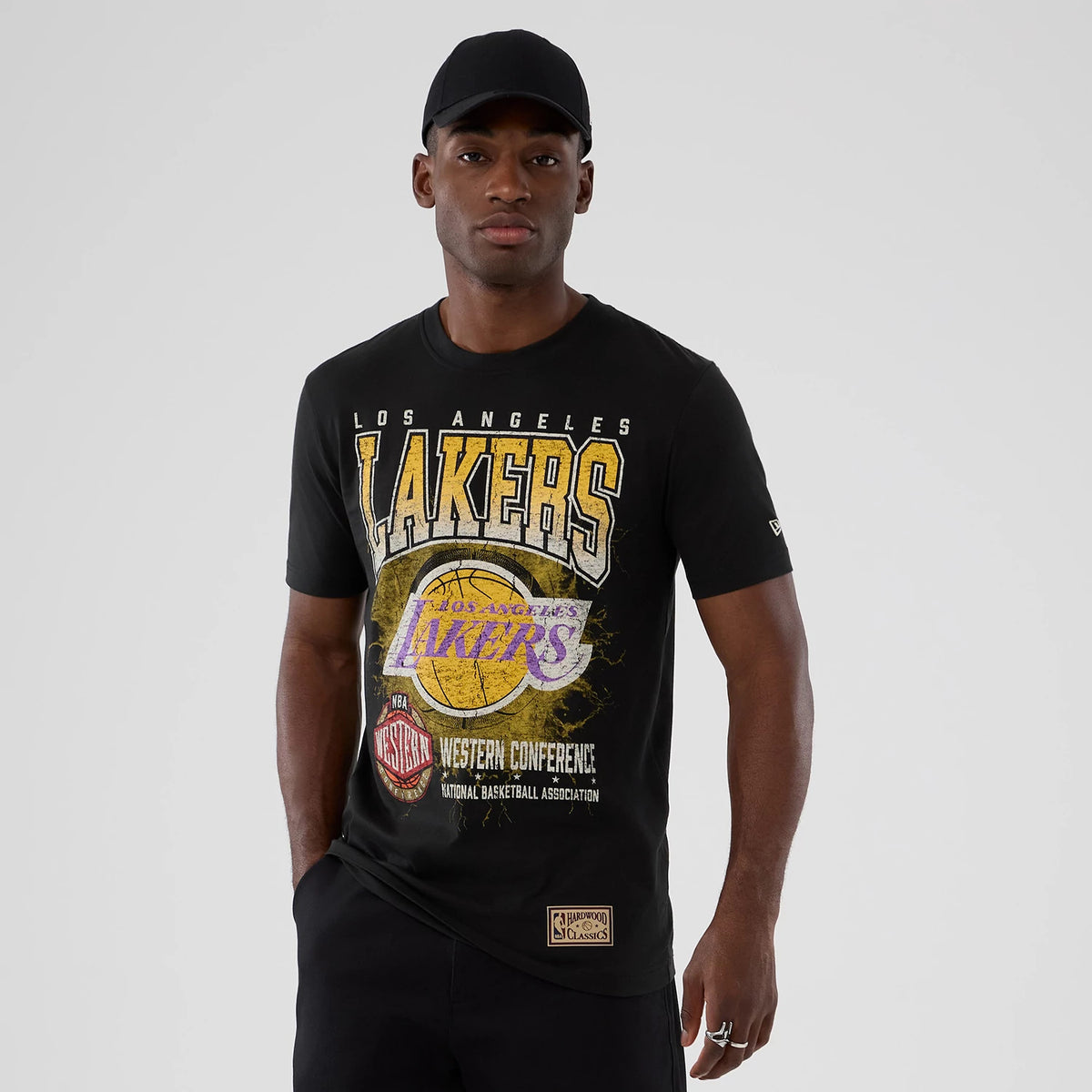 New Era LA Lakers NBA Hardwood Classic Black T-Shirt, front view on-model showing large Lakers graphic across the chest with text and a central basketball design, embroidered New Era logo on the left sleeve above the elbow.