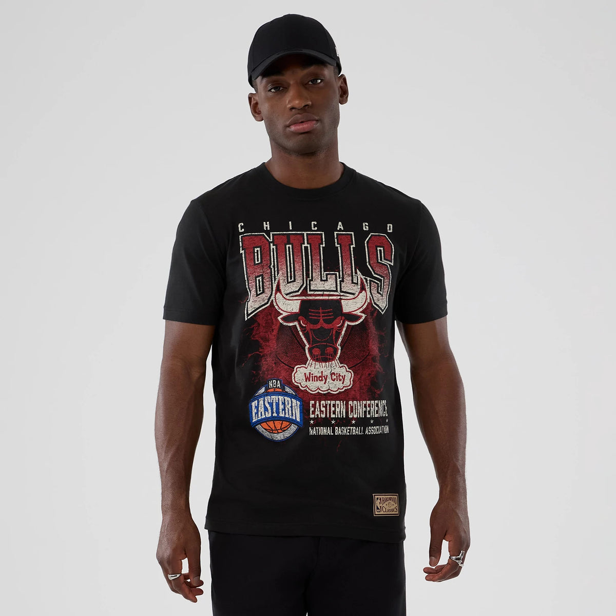 New Era Chicago Bulls NBA Hardwood Classic Black T-Shirt, front view showing a large printed Bulls graphic with Windy City text on the chest, NBA Eastern Conference graphics below, and a Hardwood Classics patch near the hem on the model's left side.