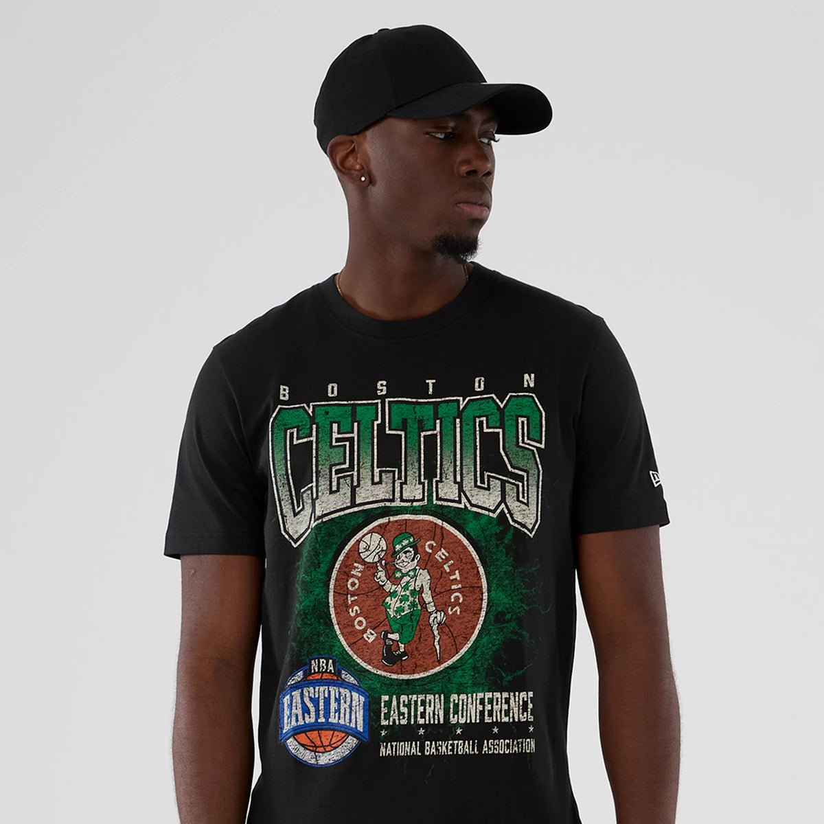 New Era Boston Celtics NBA Hardwood Classic Black T-Shirt, front view on-model showing the large Celtics graphic with lettering and a vintage basketball logo across the chest, paired with a plain black cap.
