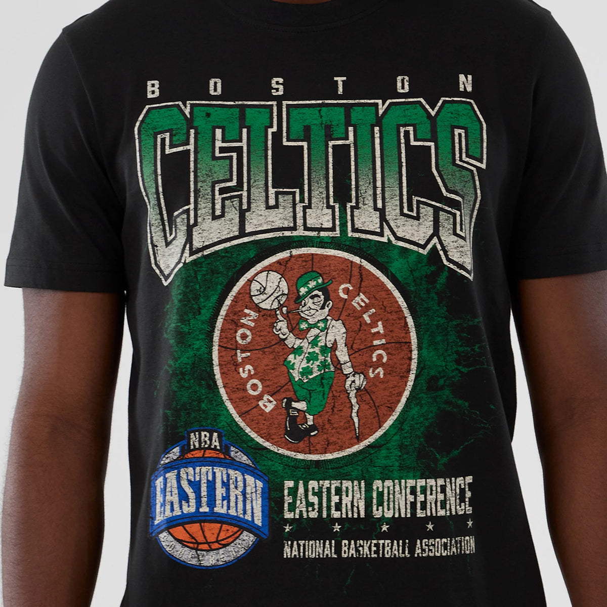 New Era Boston Celtics NBA Hardwood Classic Black T-Shirt, front view showing large distressed Celtics lettering in green and white above a Boston Celtics logo with a leprechaun, and a graphic of the NBA Eastern Conference emblem near the hem.