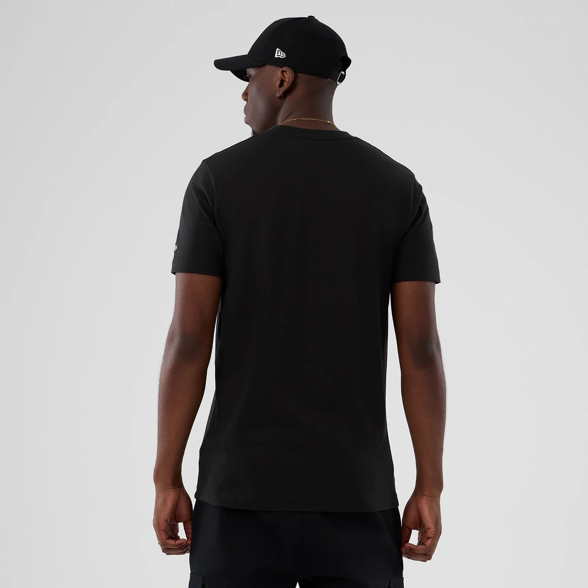New Era Boston Celtics NBA Hardwood Classic Black T-Shirt, back view on a model wearing a black New Era cap, showing the plain black rear of the tee and short sleeves with a small embroidered logo on the right arm.