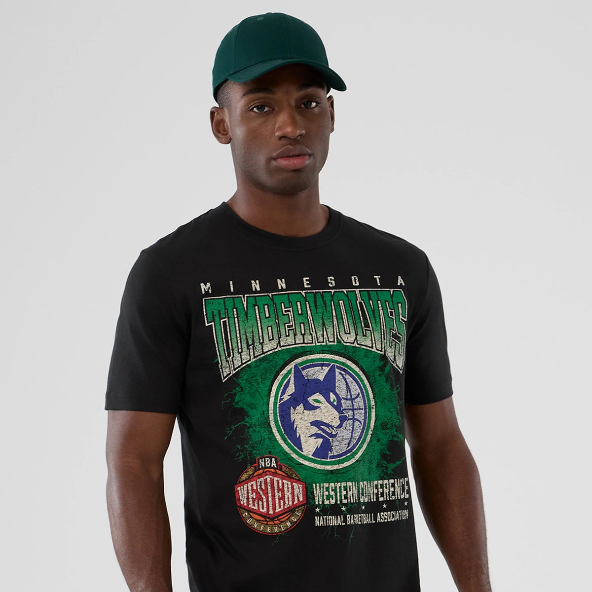 New Era Minnesota Timberwolves NBA Hardwood Classic Black T-Shirt, front view on-model showing large vintage-style Timberwolves graphic and lettering on the chest in green and white, paired with a dark green cap.