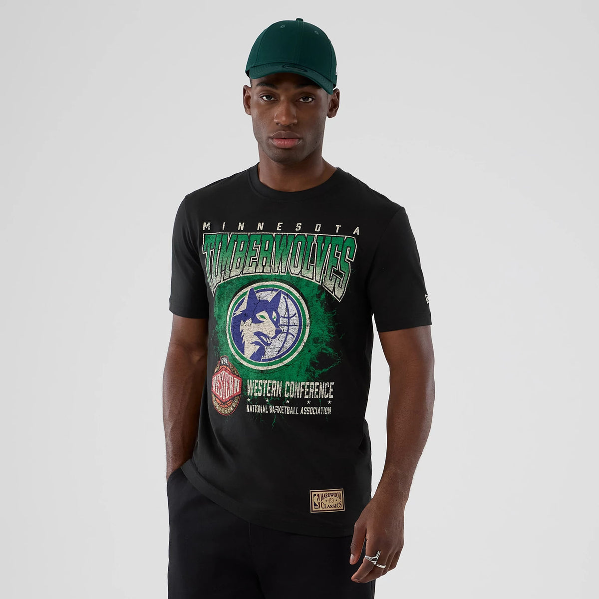 New Era Minnesota Timberwolves NBA Hardwood Classic Black T-Shirt, front view on-model showing large Timberwolves graphic in green and purple with NBA and Western Conference text in white, embroidered New Era logo on the left sleeve.