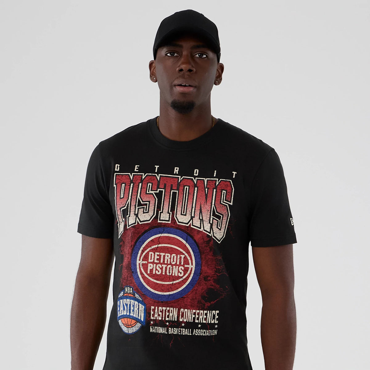 New Era Detroit Pistons NBA Hardwood Classic Black T-Shirt, front view on-model showing large distressed Pistons graphic with basketball and Eastern Conference lettering, featuring an embroidered New Era logo on the sleeve.