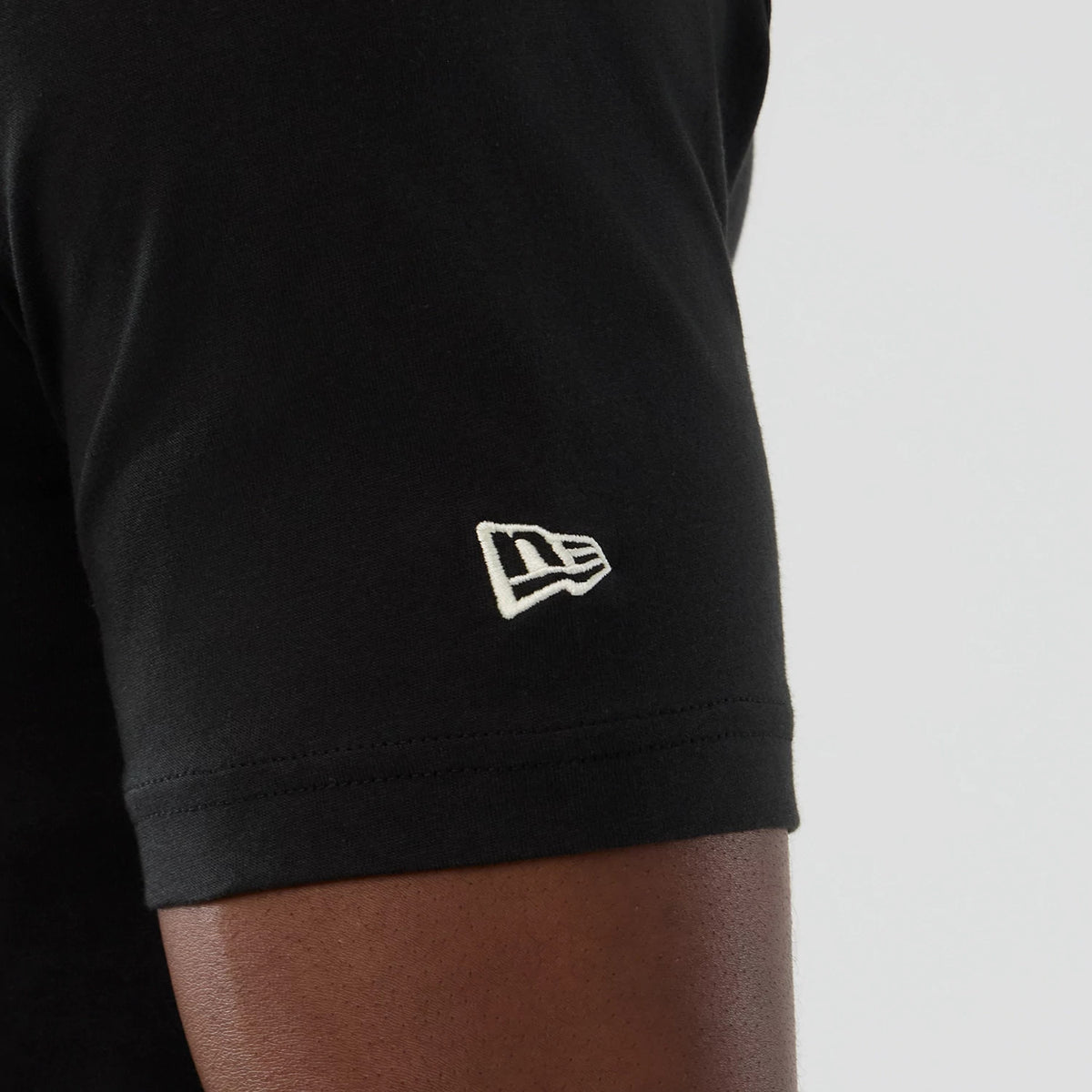 New Era Dallas Mavericks NBA Hardwood Classic Black T-Shirt, side view focusing on the short sleeve with a white embroidered New Era logo positioned near the hem, highlighting the clean black fabric of the tee.