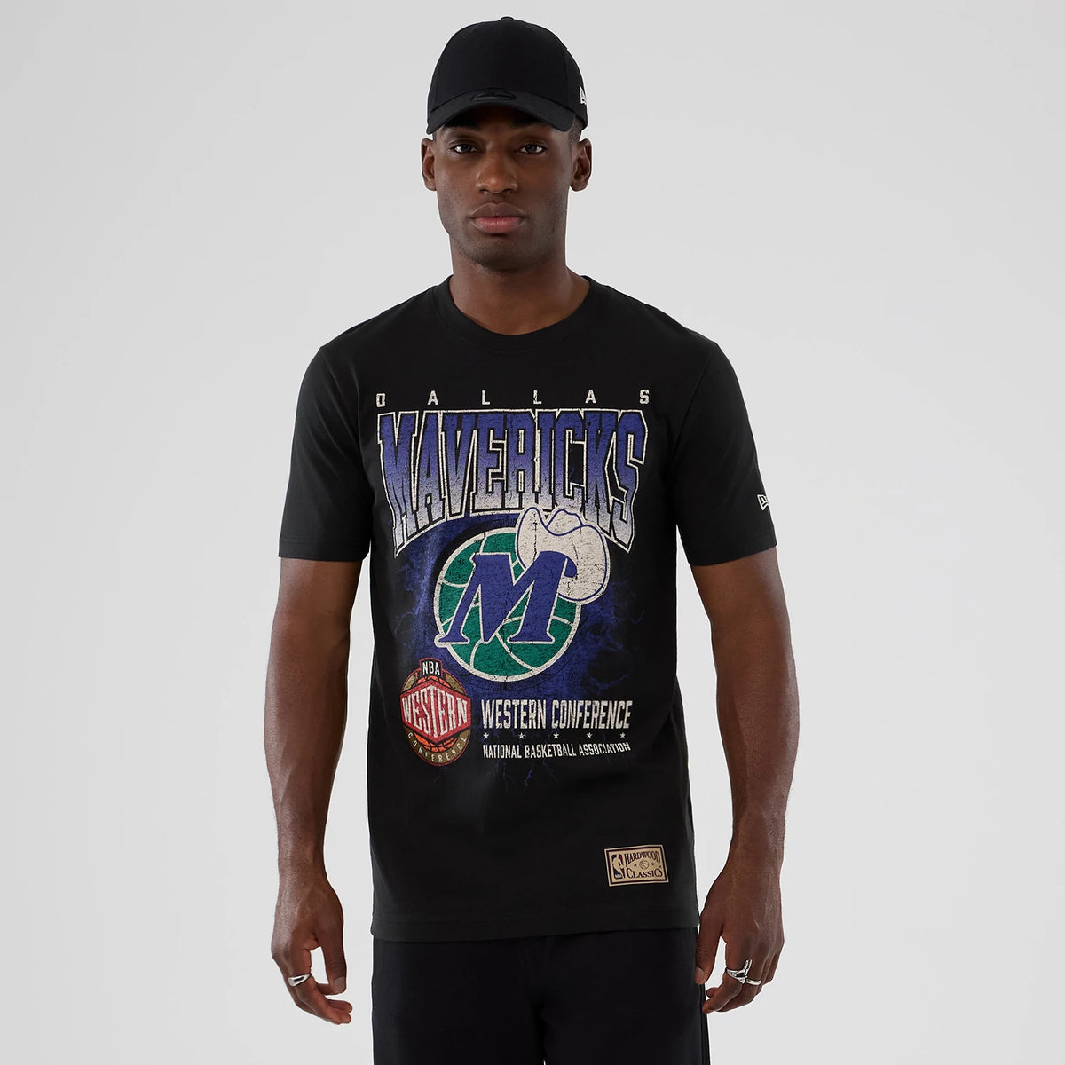 New Era Dallas Mavericks NBA Hardwood Classic Black T-Shirt, front view on-model showcasing the Mavericks graphic printed across the chest in blue and green, New Era logo embroidered on the left sleeve, styled with a black cap.