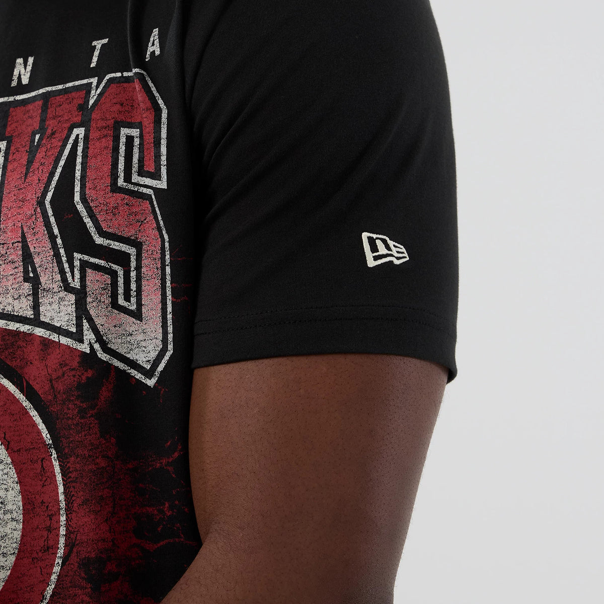 New Era Atlanta Hawks NBA Hardwood Classic Black T-Shirt, side view showing the Hawks team lettering in red and white on the black fabric, with a small white embroidered New Era logo on the sleeve near the edge.