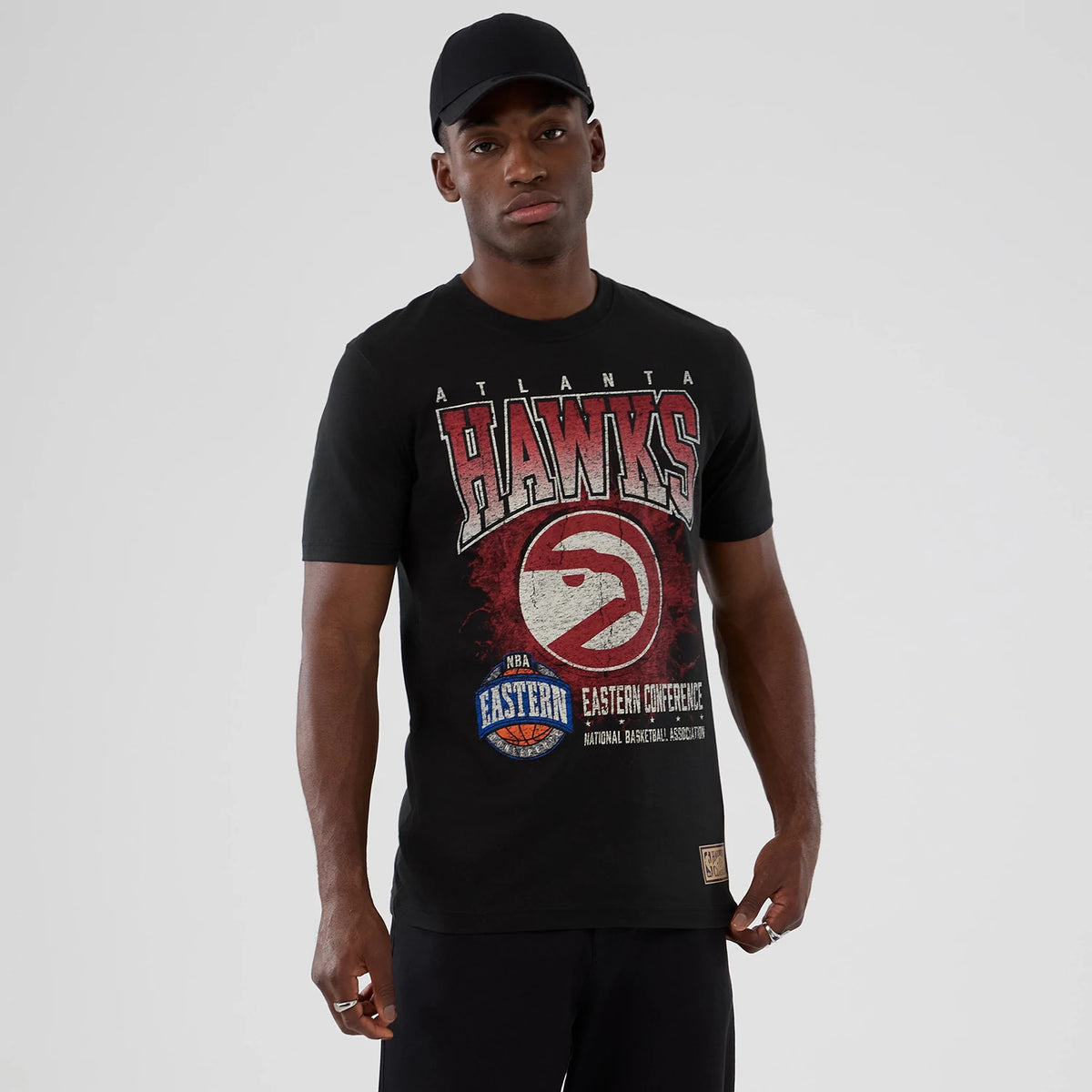 New Era Atlanta Hawks NBA Hardwood Classic Black T-Shirt, front view on-model showing large distressed Hawks logo and lettering across the chest, with additional NBA Eastern Conference graphics and a small woven label at the hem.