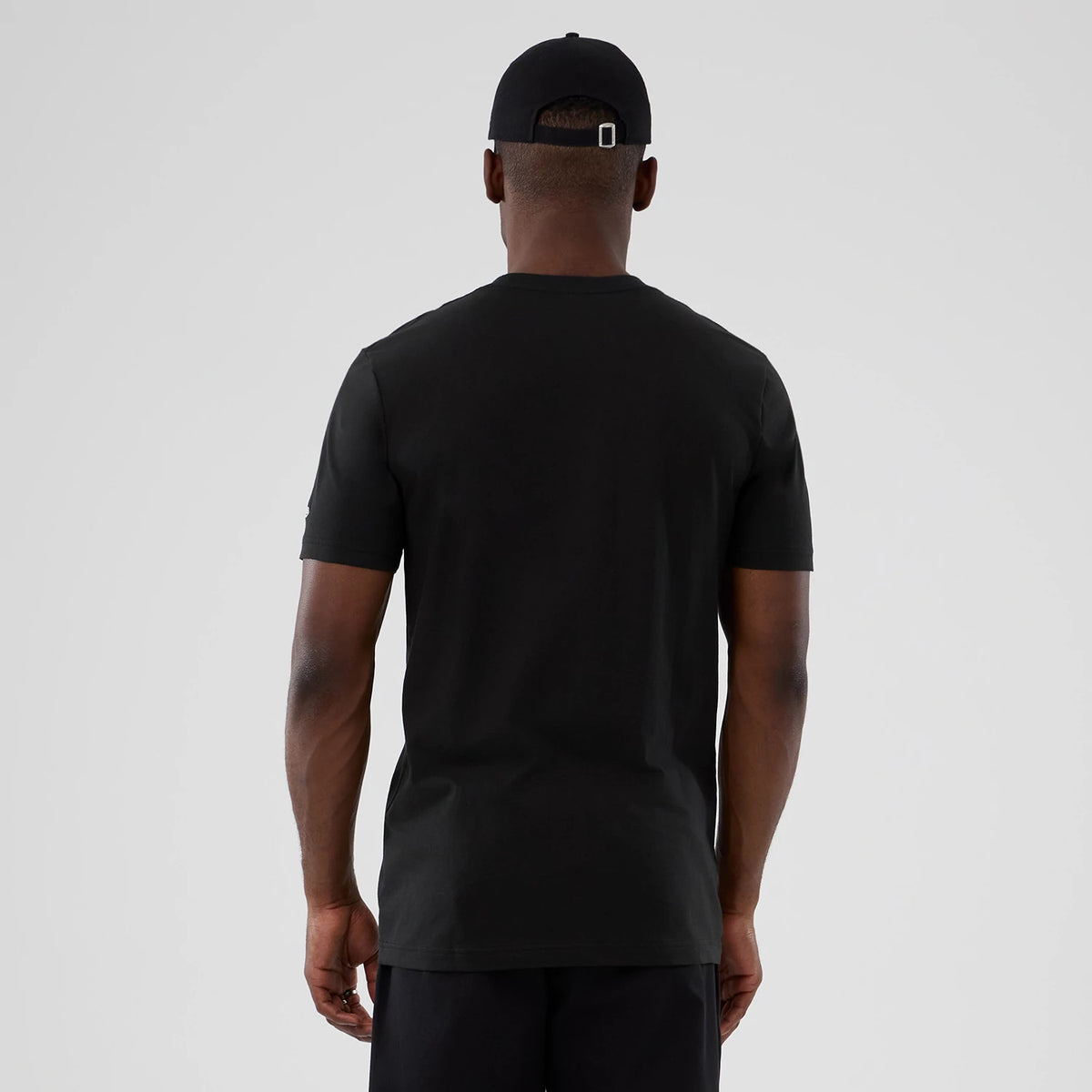 New Era Atlanta Hawks NBA Hardwood Classic Black T-Shirt, back view showing a plain black design with a round neckline on a model, paired with a black cap, presenting a and minimal look.