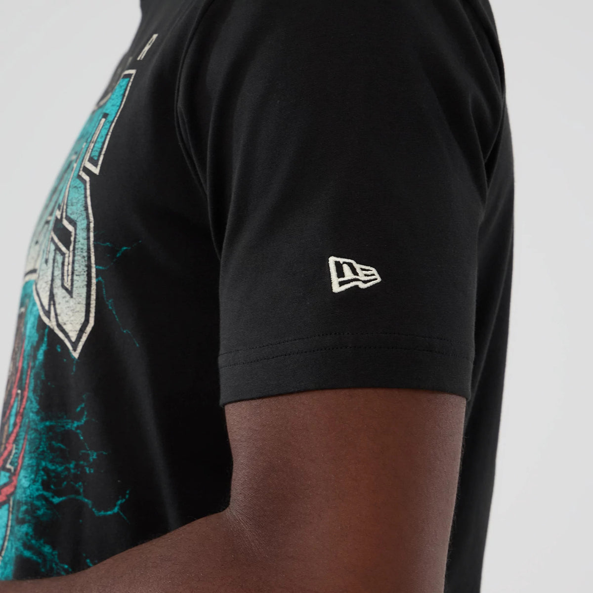 New Era Vancouver Grizzlies NBA Hardwood Classic Black T-Shirt, side view showing the sleeve with a white embroidered New Era logo, and part of the front graphic featuring teal and white design details.