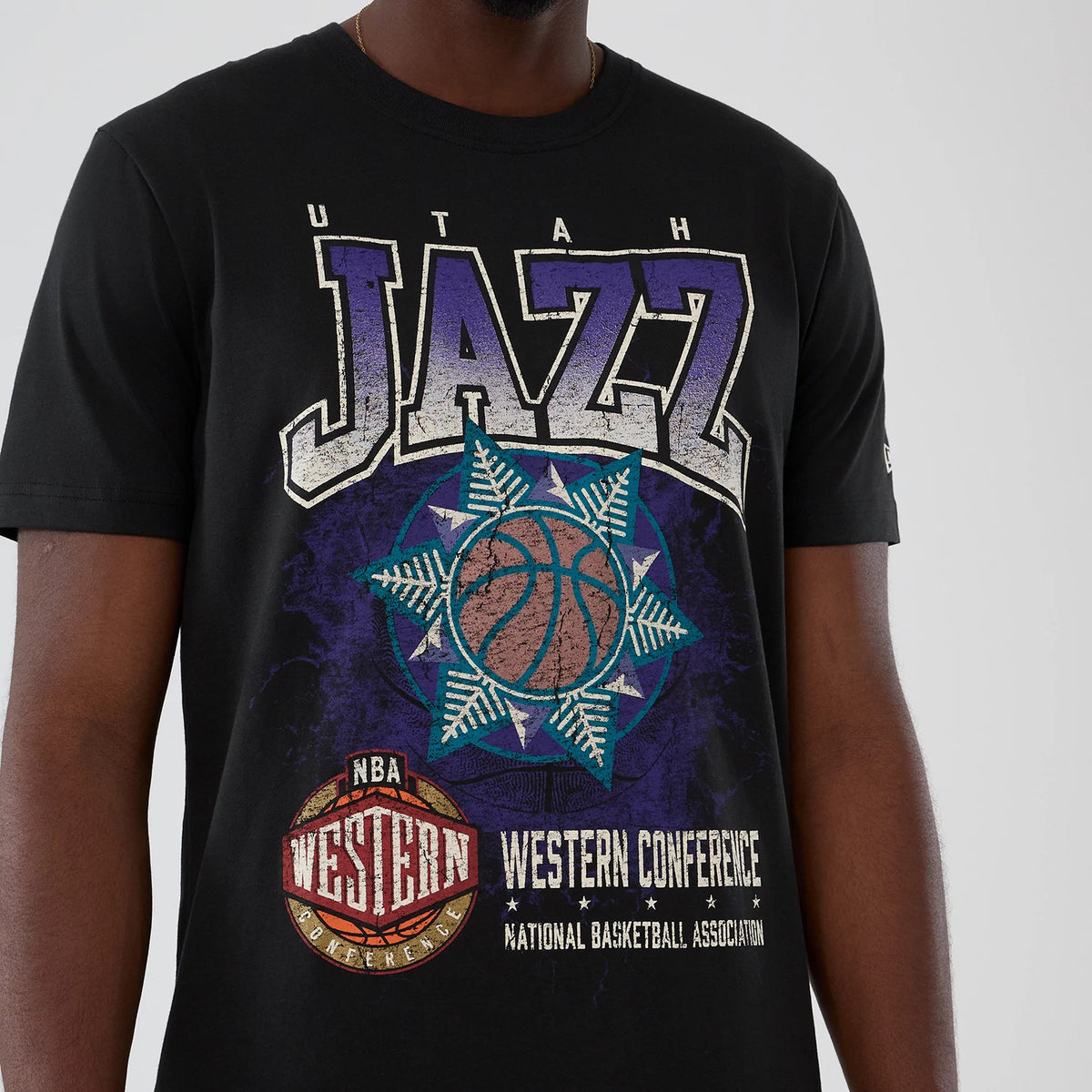 New Era Utah Jazz NBA Hardwood Classic Black T-Shirt, front view on-model showing a large printed Utah Jazz logo with a basketball graphic and Western Conference emblem across the chest, and a small embroidered New Era logo on the left sleeve.